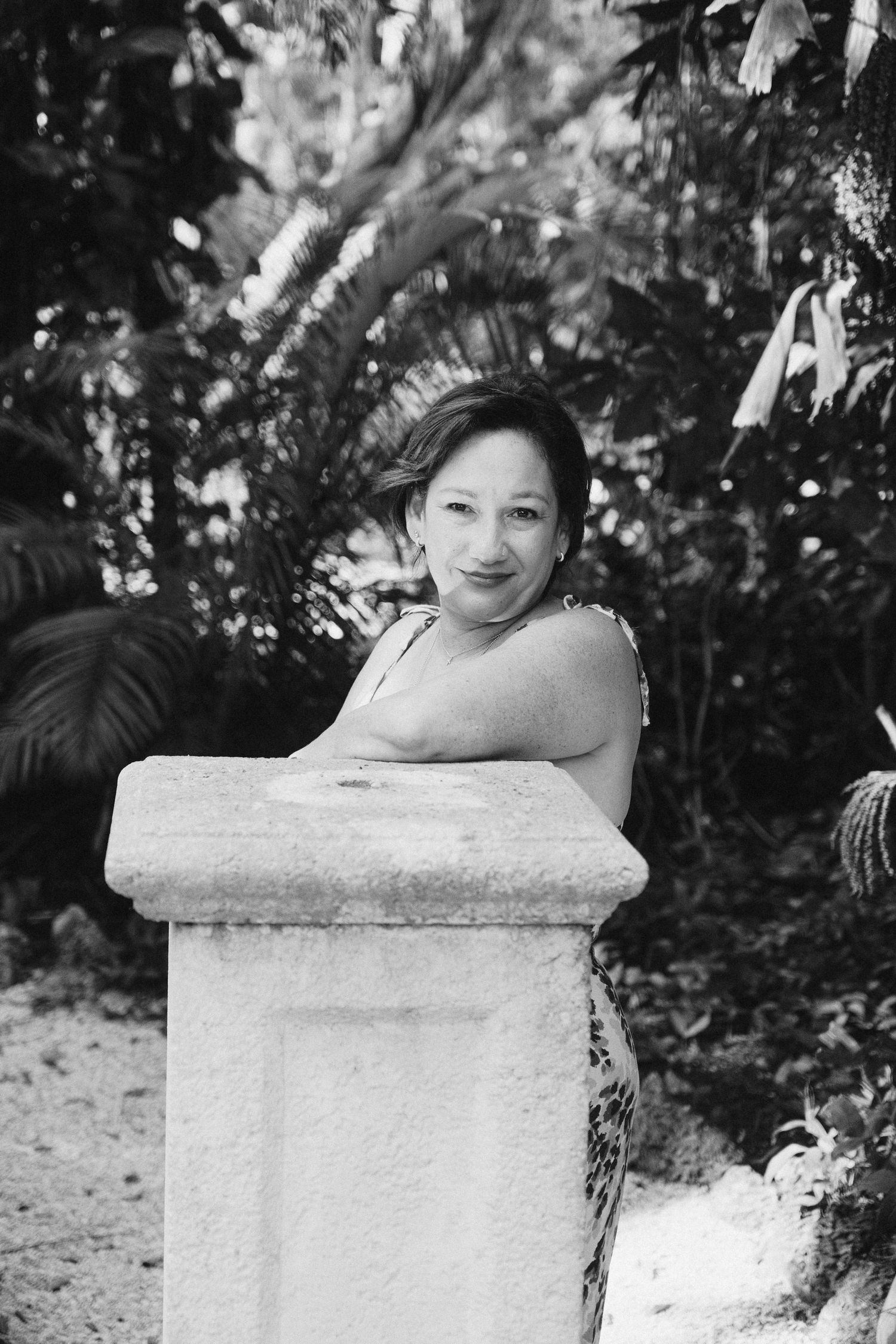 Black and white artistic portrait series showing someone posing by a stone pillar in a garden setting.