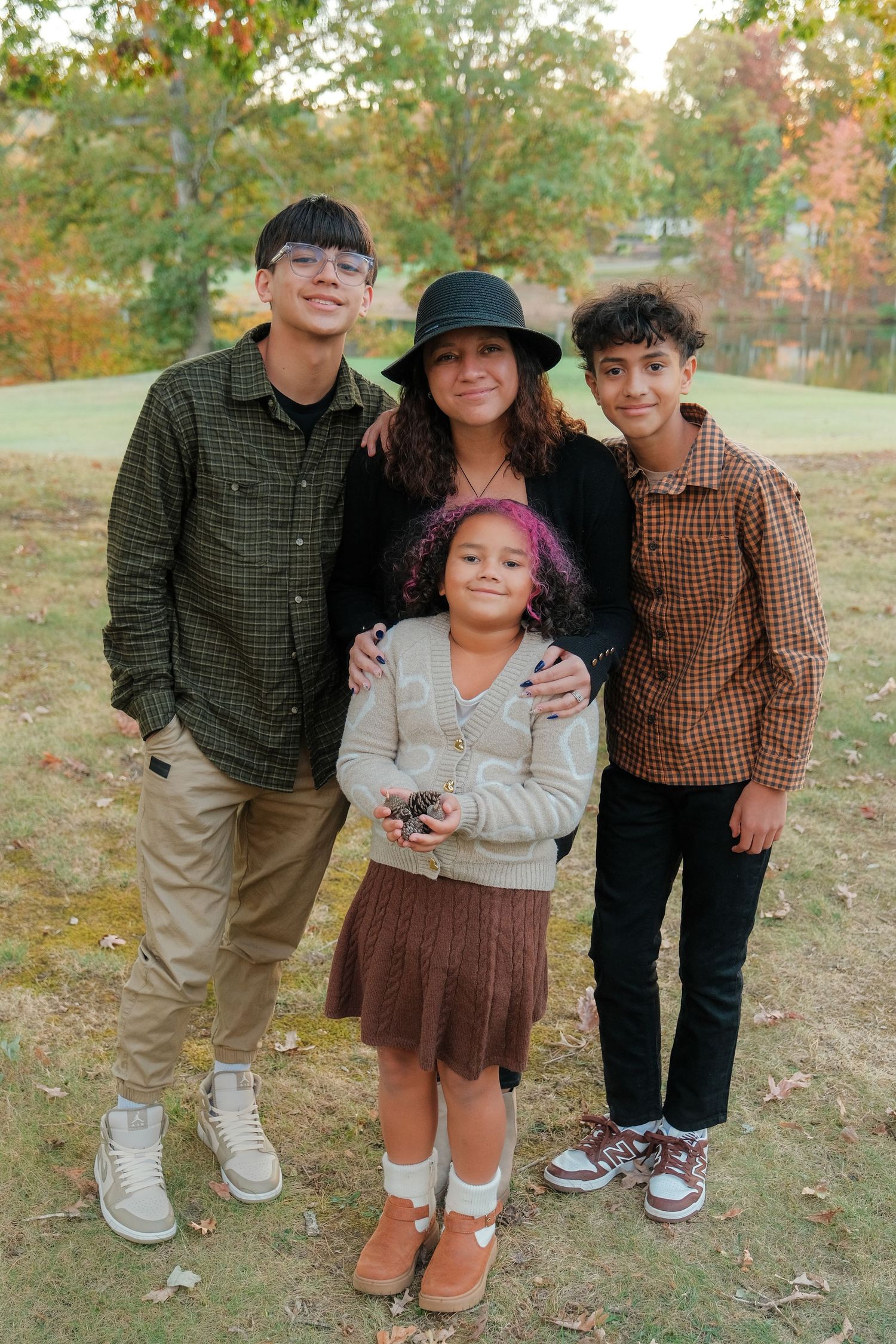 A family poses together outdoors during autumn with fallen leaves and trees in the background.