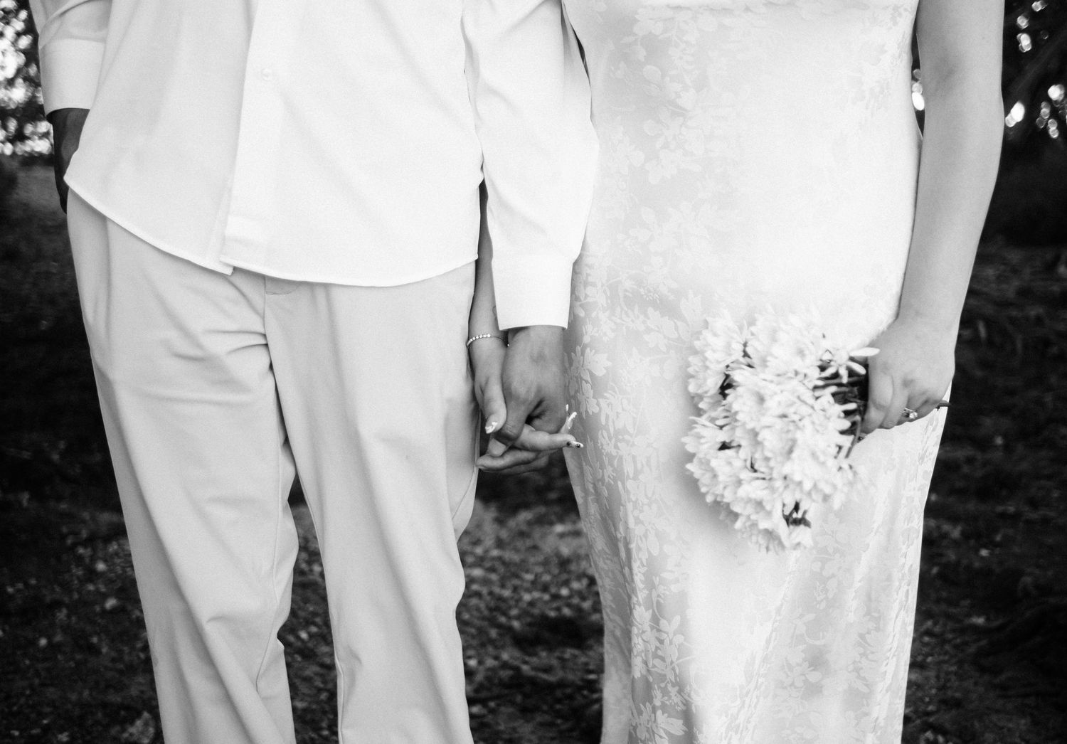 Wedding party members in white attire stand together holding floral bouquets outdoors.