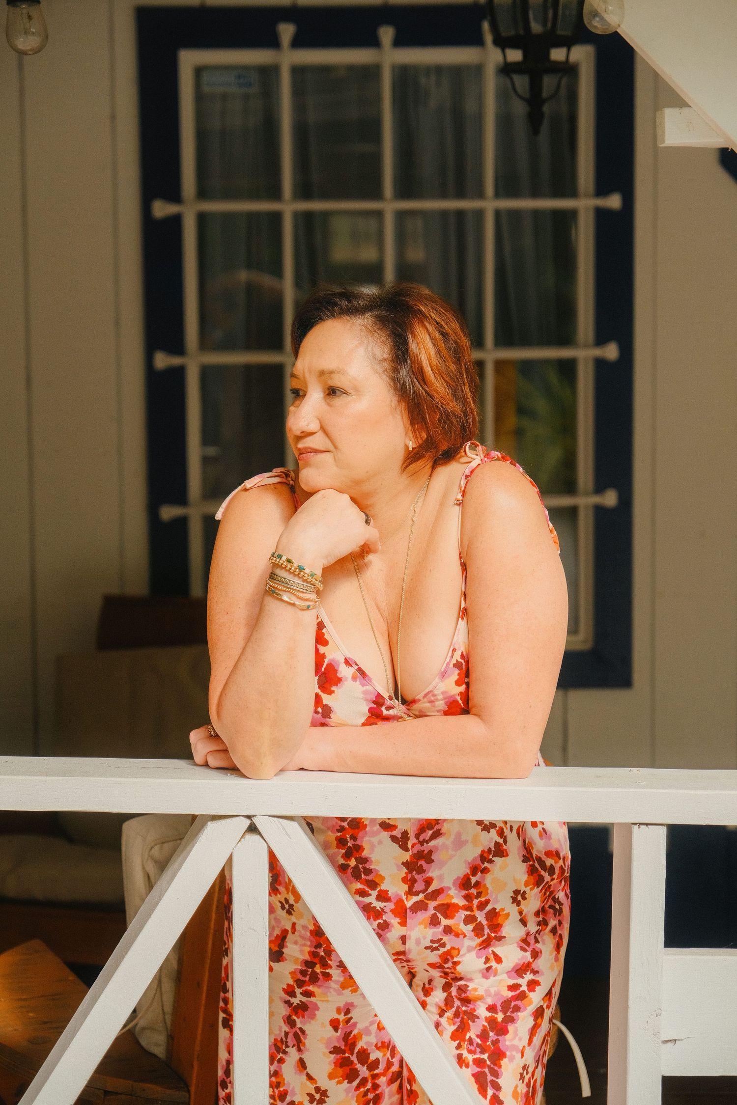 A person in a red and white floral dress leans on a white railing during a sunset photoshoot.