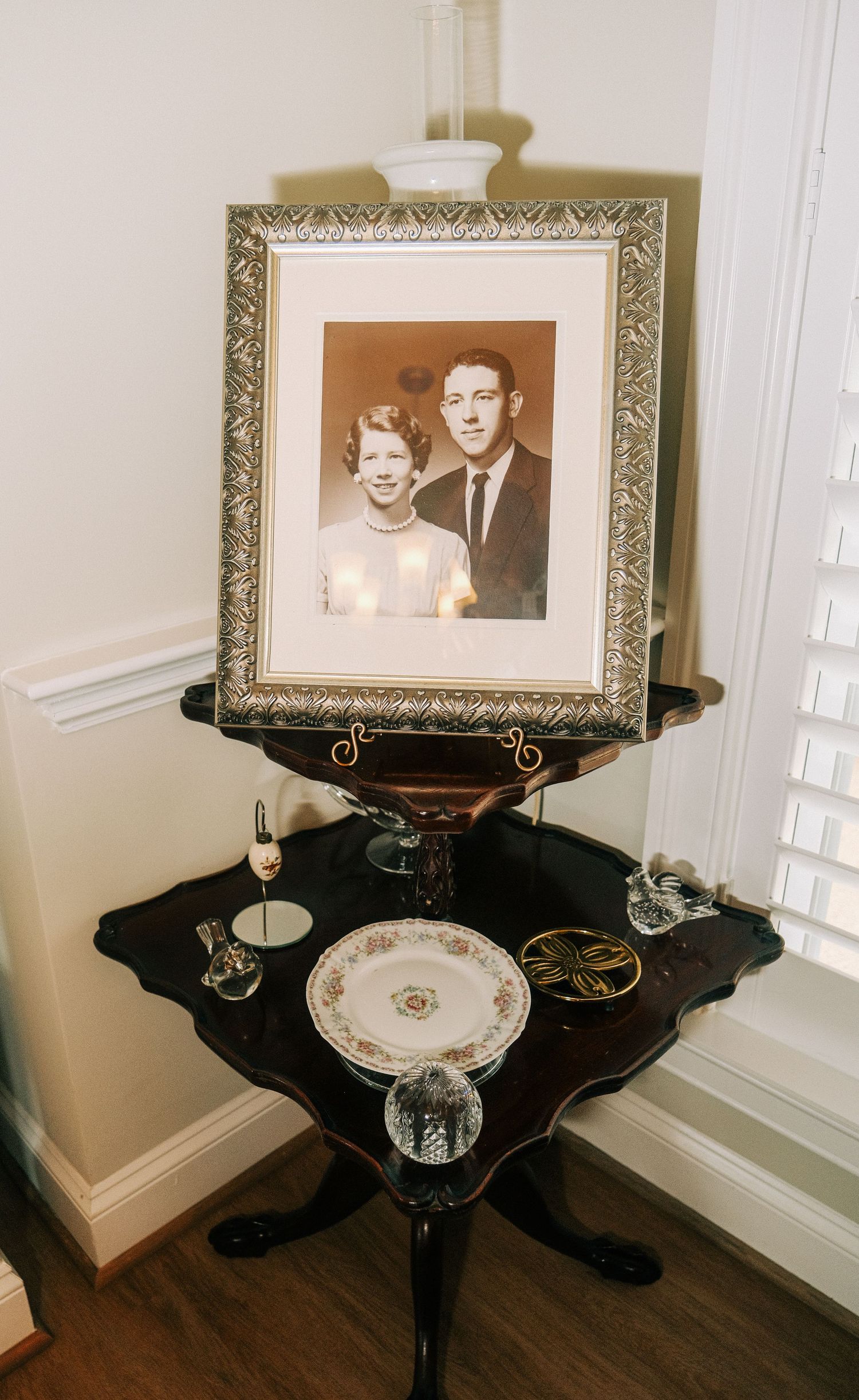 Vintage black and white couple portrait in ornate silver frame displayed on antique table with crystal and china.