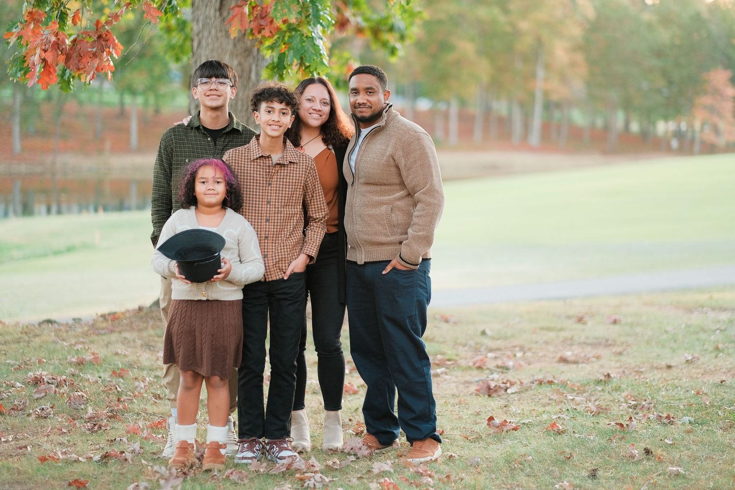 A group of people pose together outdoors in coordinating brown and black outfits during autumn.
