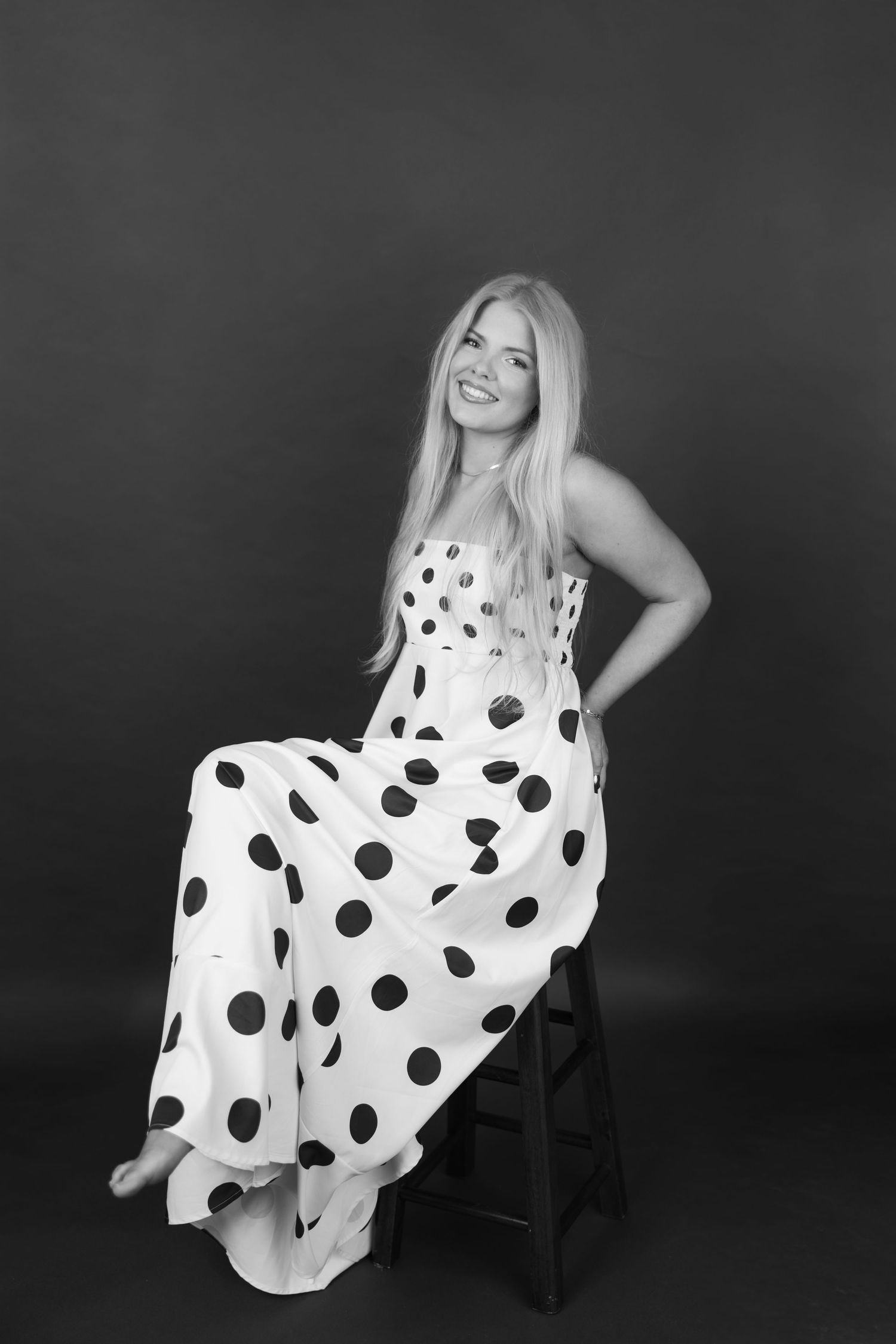 Person in casual attire poses on wooden stool against white backdrop in lifestyle photoshoot series.