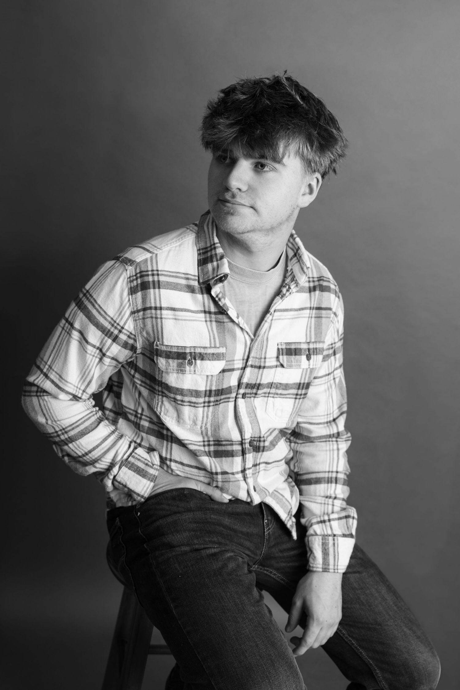 Person in plaid button-down and jeans poses dramatically in black and white portrait series.