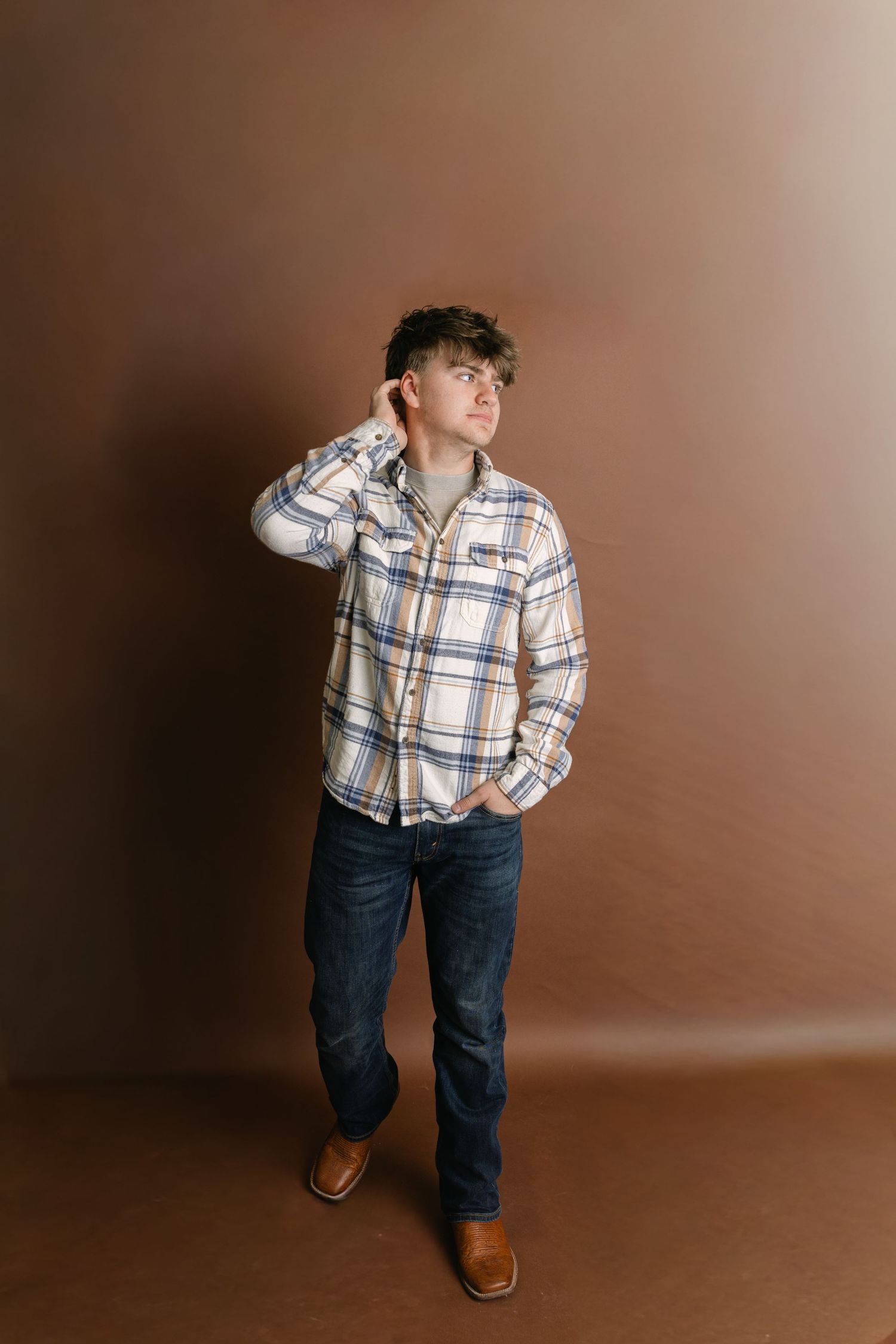 Child wearing plaid shirt and jeans strikes playful poses against brown backdrop.