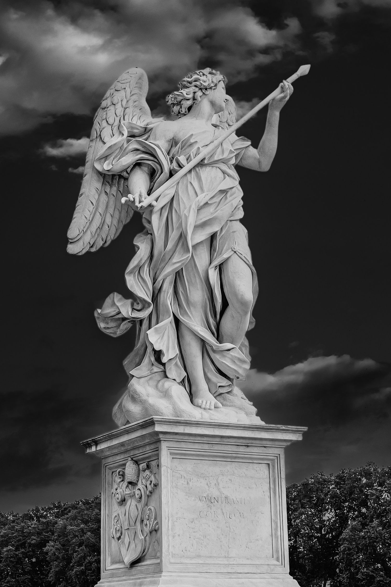 Black and white photo of an angel statue holding a lance on Ponte Sant'Angelo bridge in Rome, Italy.