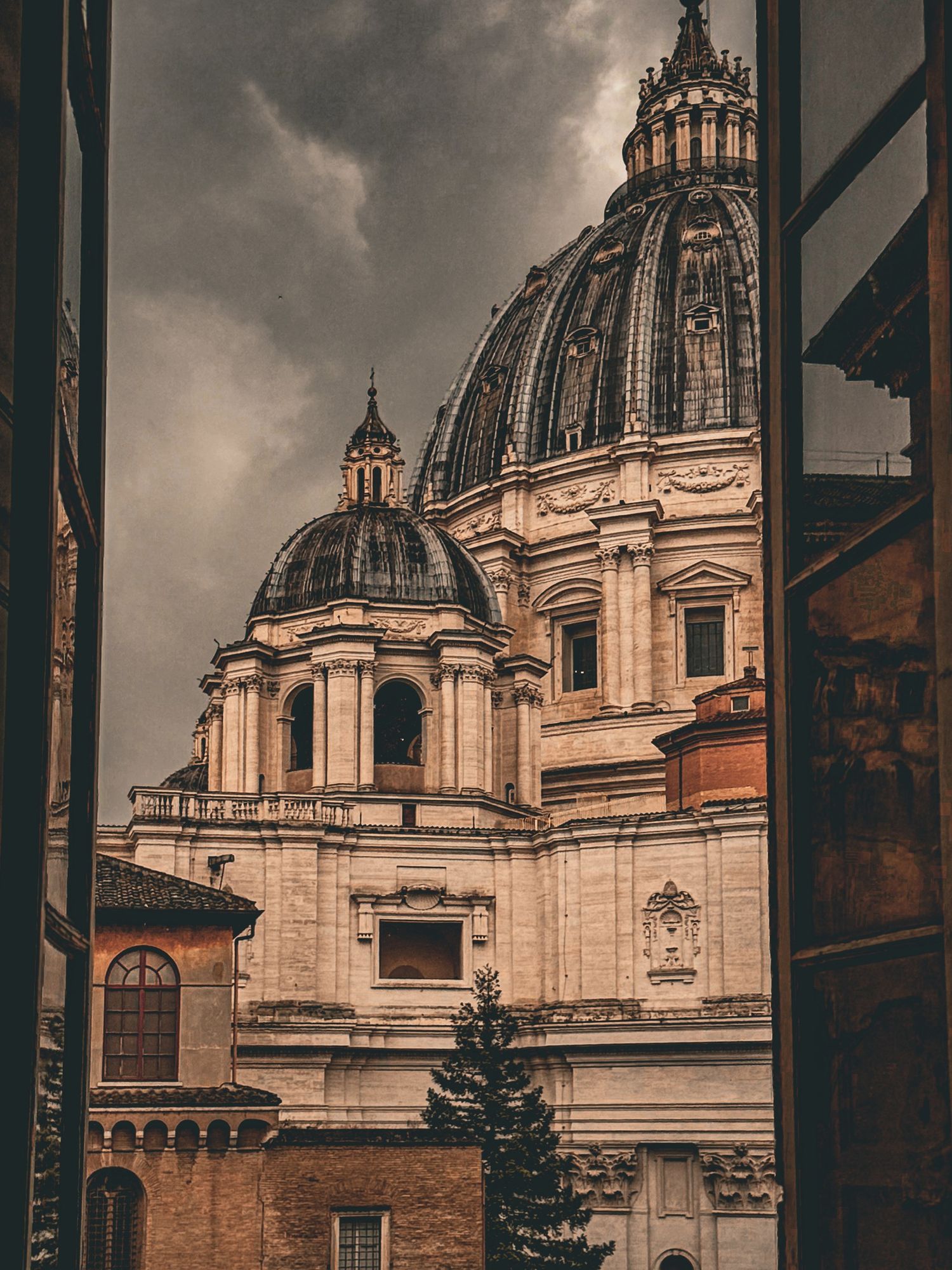 Dramatic view of St. Peter's Basilica dome in Vatican City framed by buildings under stormy skies.