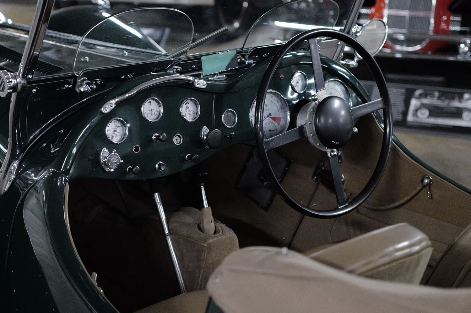 Vintage classic car interior featuring a dark green dashboard with gauges, black steering wheel, and gear shift in a museum setting.