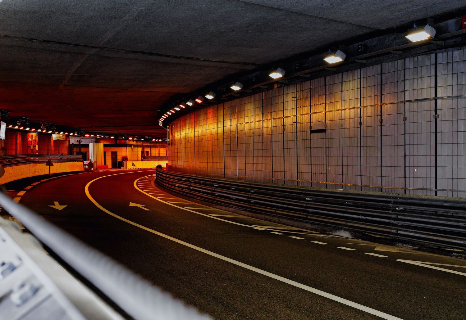 Empty curved tunnel road with orange-lit walls, ceiling lights, and lane markings in a modern highway underpass.