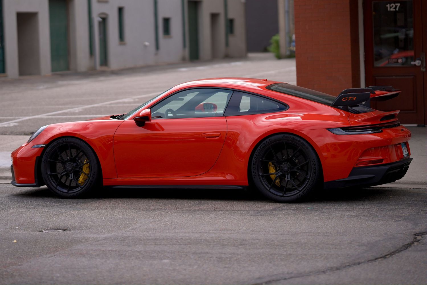 Red Porsche 911 GT3 sports car parked on a city street, featuring a large rear wing and black alloy wheels.