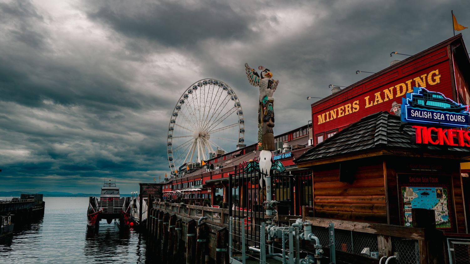 Panoramic view of a seaside amusement park pier with Ferris wheel under stormy skies.