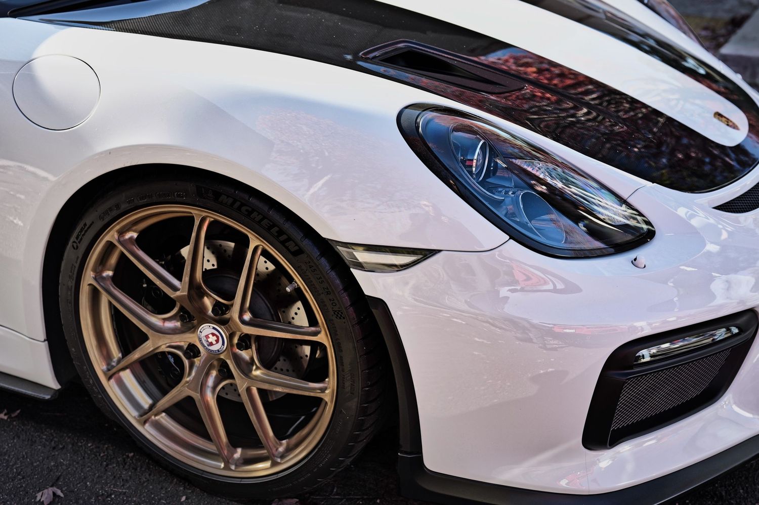 White Porsche sports car with bronze alloy wheels and sleek headlight detail on display.