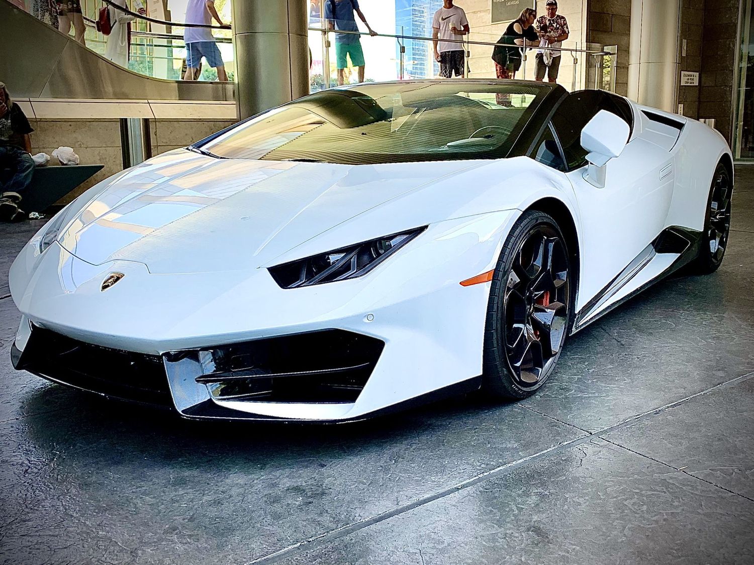 White Lamborghini Huracan Spyder convertible sports car on display indoors with glossy finish and black alloy wheels.