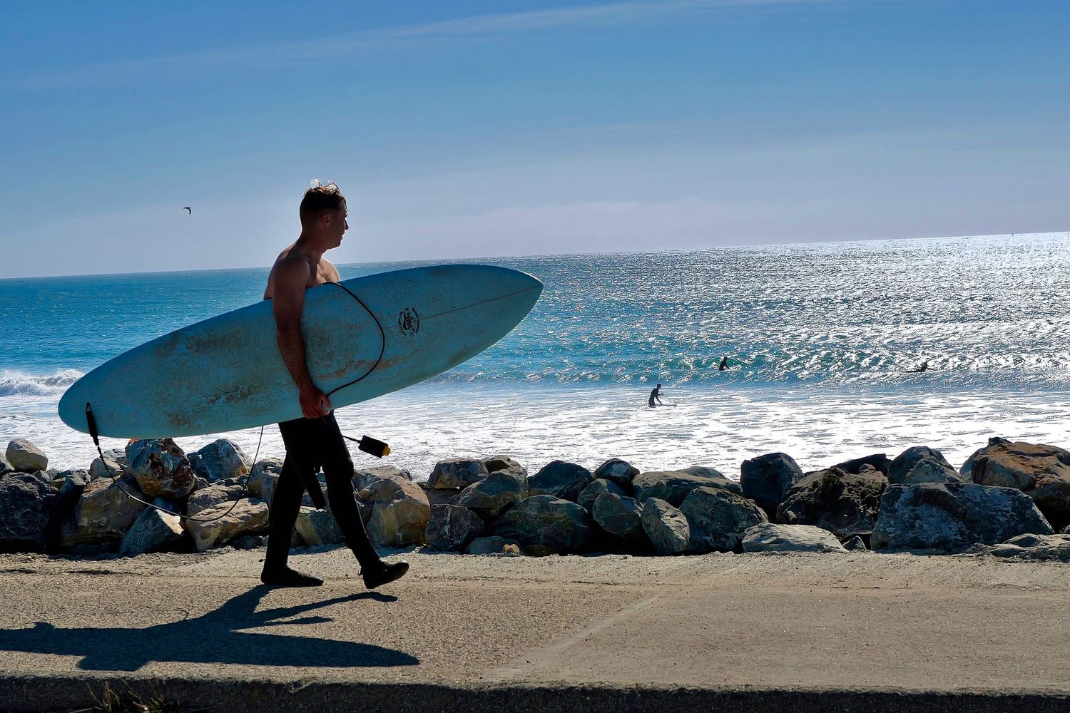 Silhouette of surfer carrying board along scenic beach at sunset.