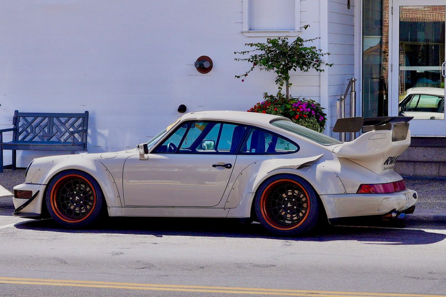 White Porsche 911 Turbo with large rear spoiler and red wheels parked on a street.