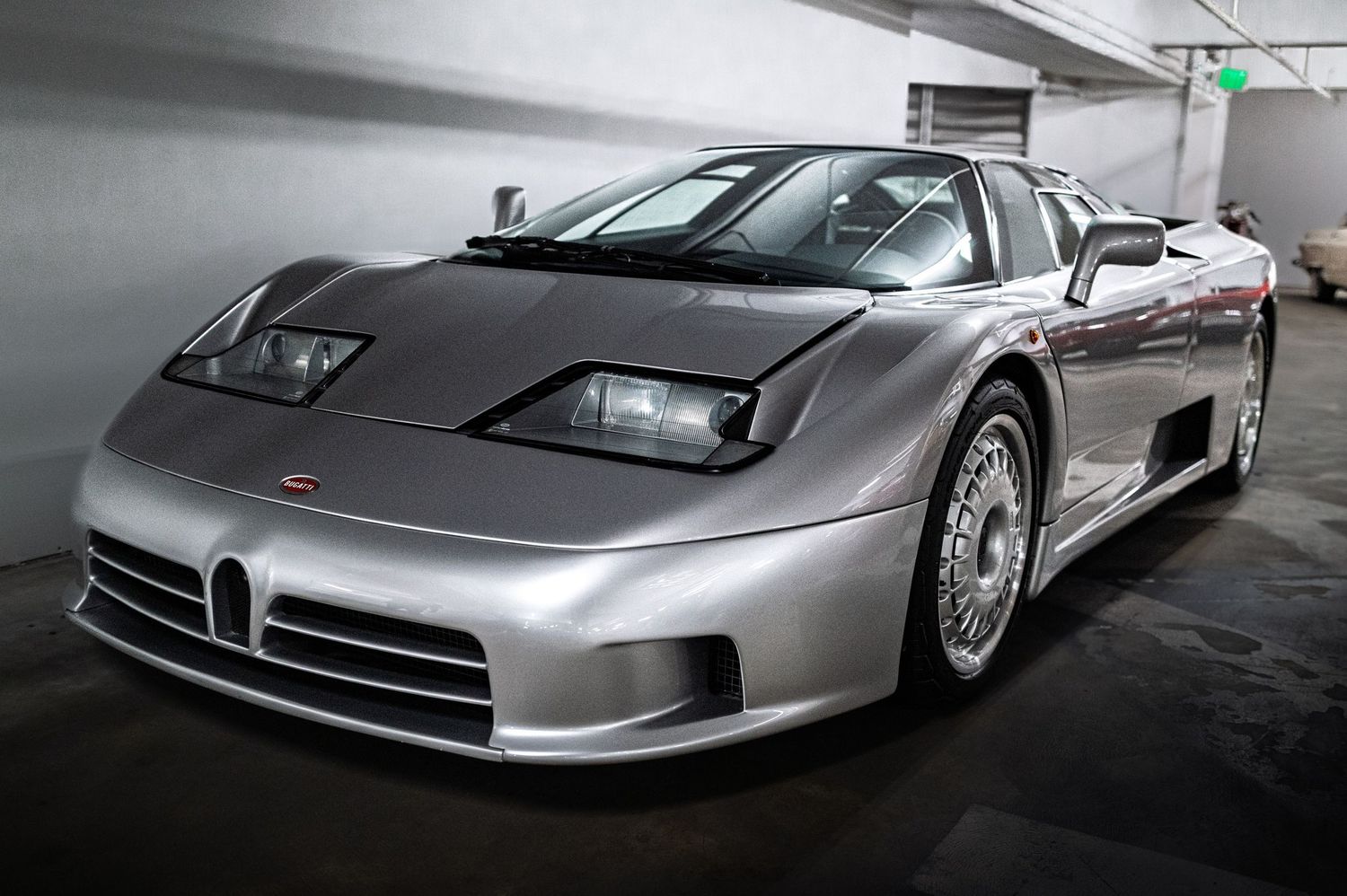 A sleek silver Bugatti EB110 supercar parked indoors, showcasing its iconic low-profile aerodynamic design and alloy wheels.