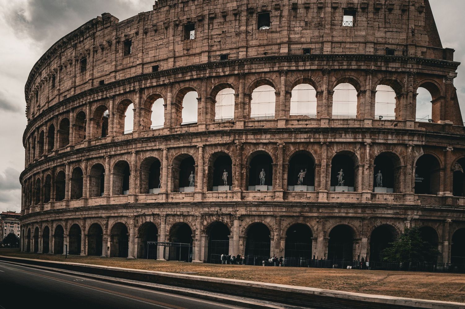 The ancient Colosseum in Rome, Italy, showcasing its iconic arched facade and weathered brick exterior under a cloudy sky.