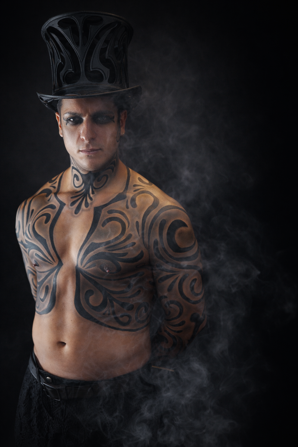 Dramatic black and white portraits showcase intricate tribal tattoos on a person's upper body against a smoky backdrop.