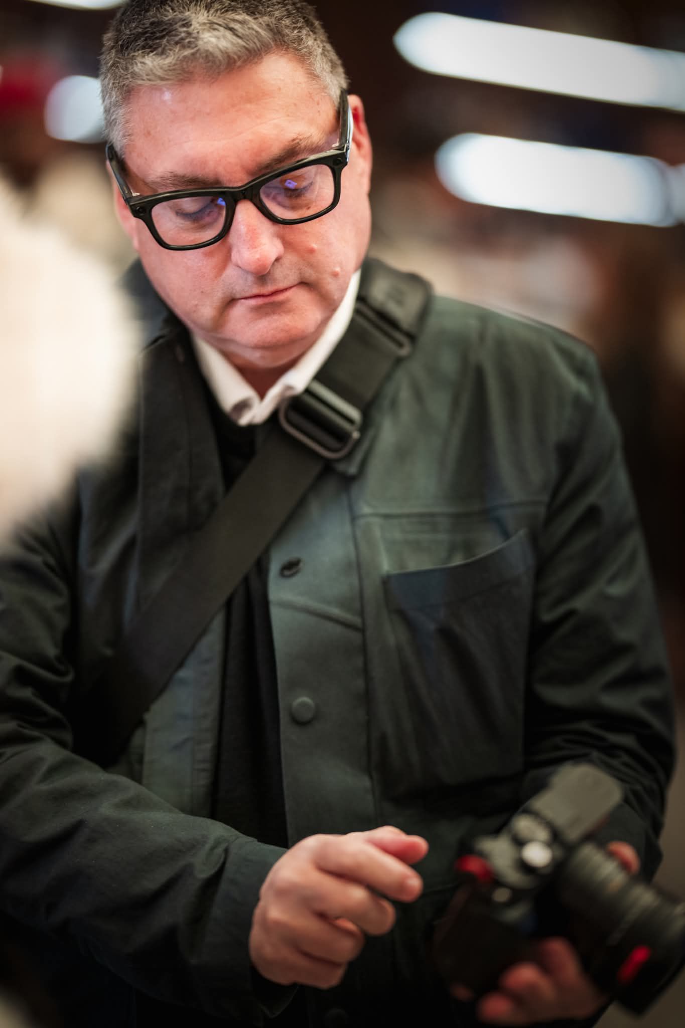 Jason Lynch in a dark coat and glasses looking at images with model on a Leica camera.