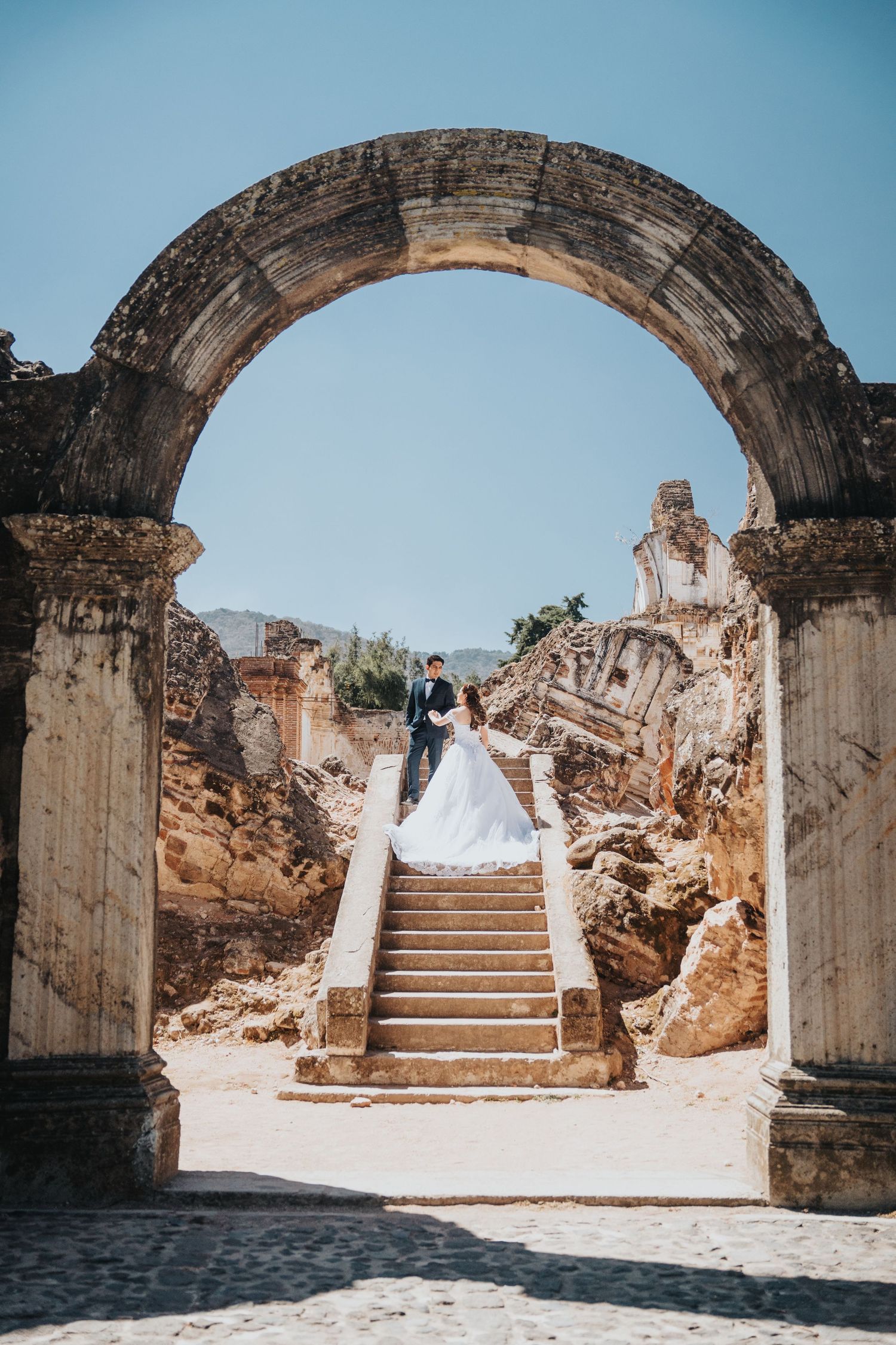 Novia y acompañante posando bajo arcos de ruinas históricas en Antigua Guatemala / Bride and companion posing under historic arches in Antig