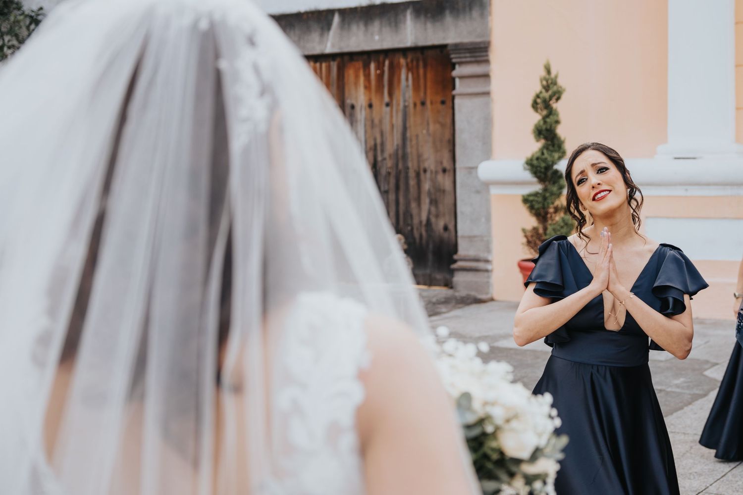 Novia con velo junto a dama de honor en vestido azul, momentos previos a la ceremonia de boda / Bride with veil standing next to bridesmaid