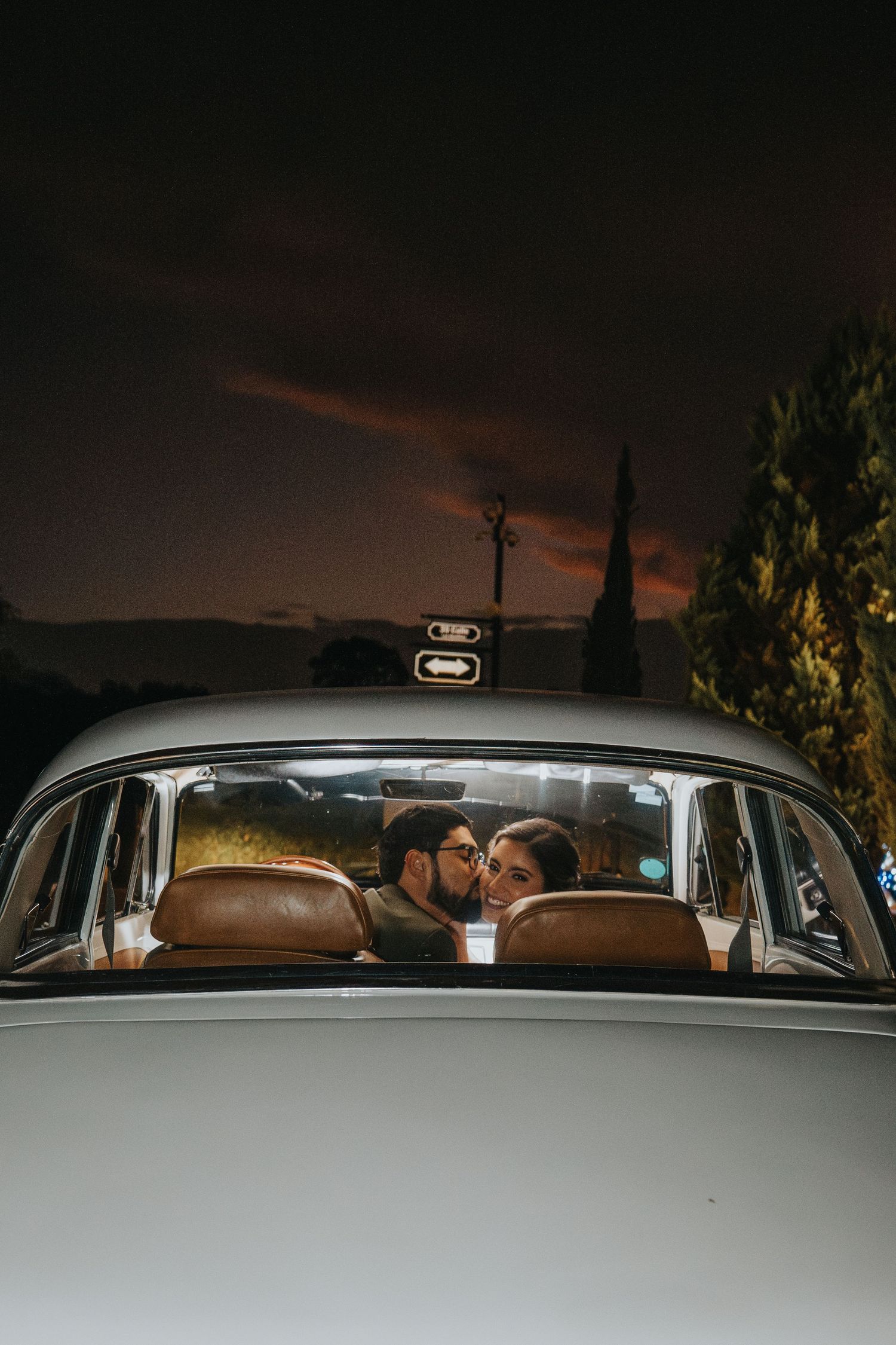 Pareja de novios besándose dentro de auto clásico vintage durante boda de noche en Antigua Guatemala - Flashlight Studio