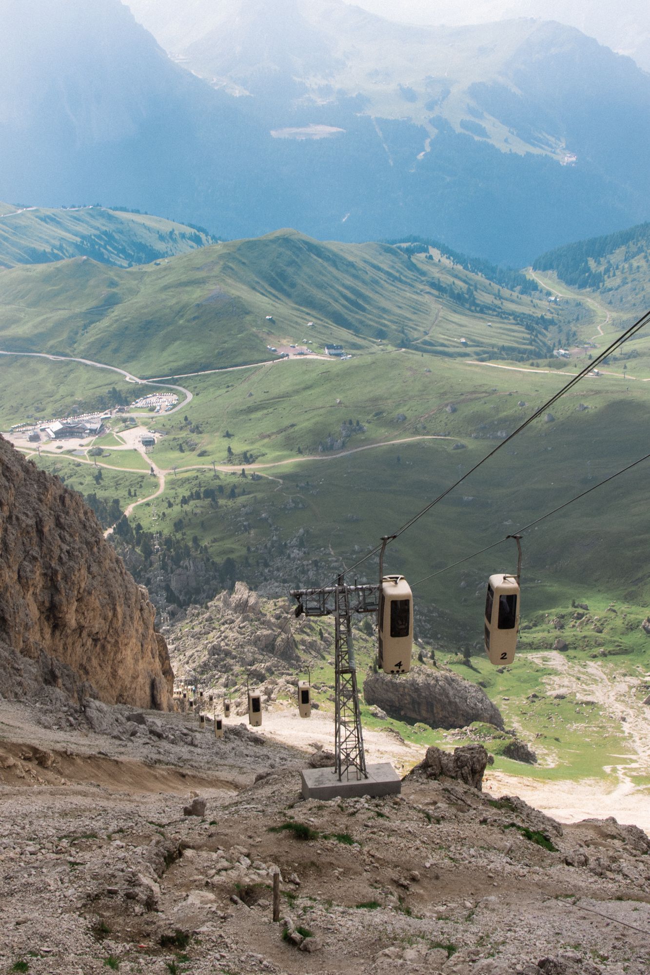 Capture the scale of the Italian Dolomites with this dramatic shot of the vintage Sassolungo cable car descending over lush alpine valleys.