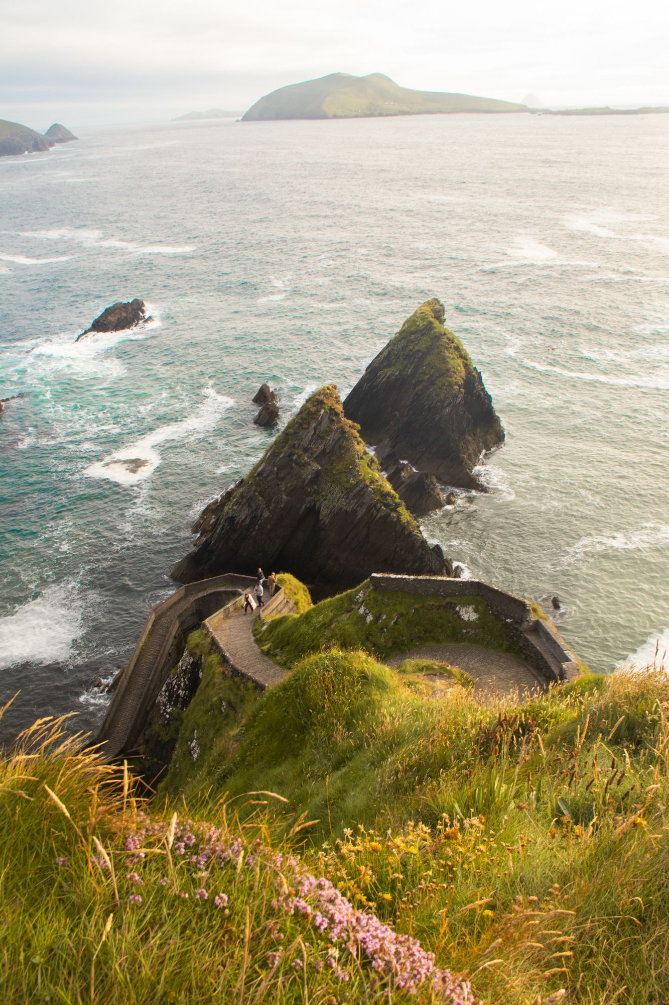 Coastal study of Dunquin Pier. Focus on the rhythmic, jagged sea stacks and the winding path against the Atlantic swell. Monumental scale.