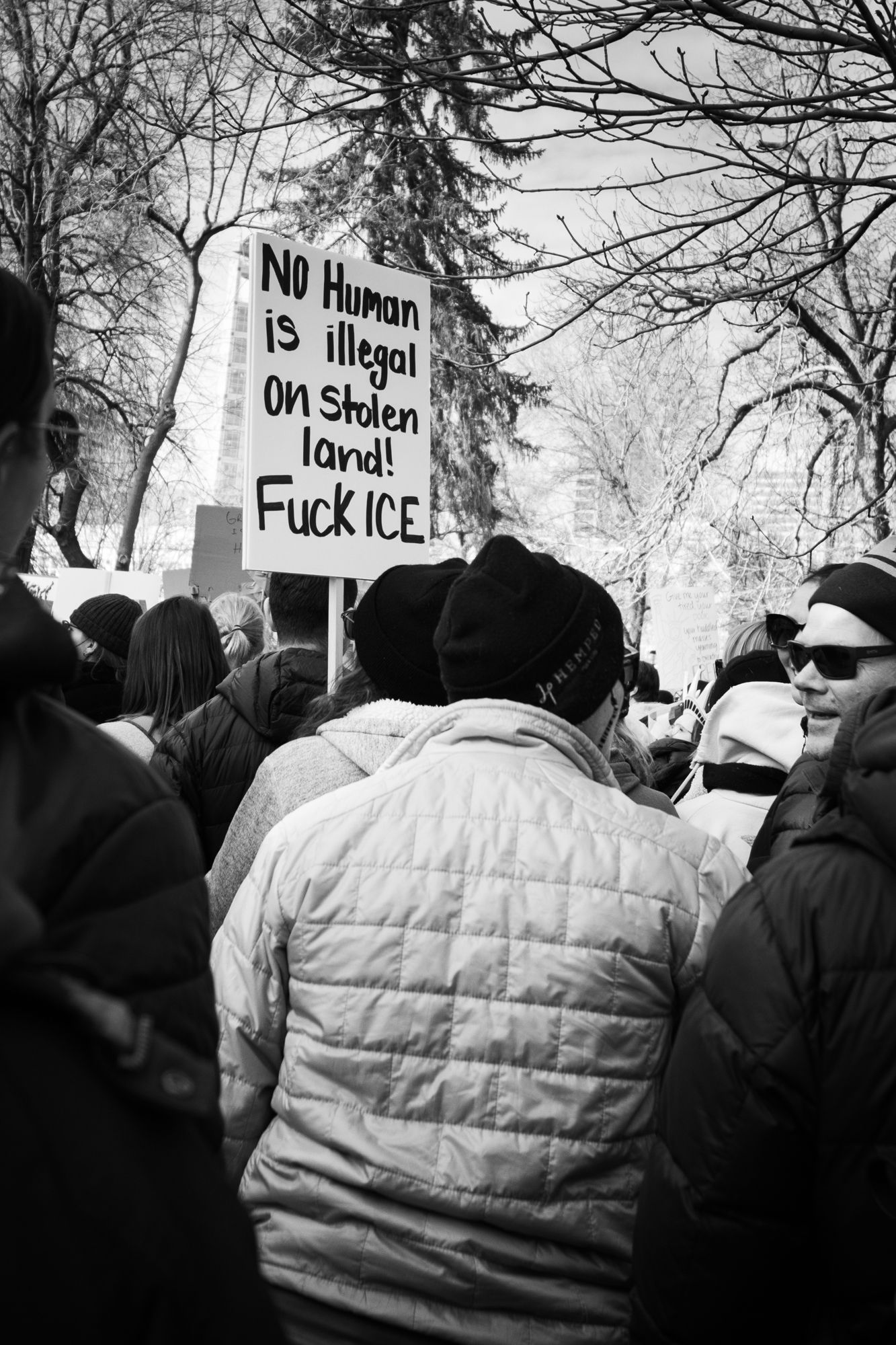 Powerful B&W documentary photography of a public protest. Handwritten sign with a personal message in a city crowd. Authentic news imagery.