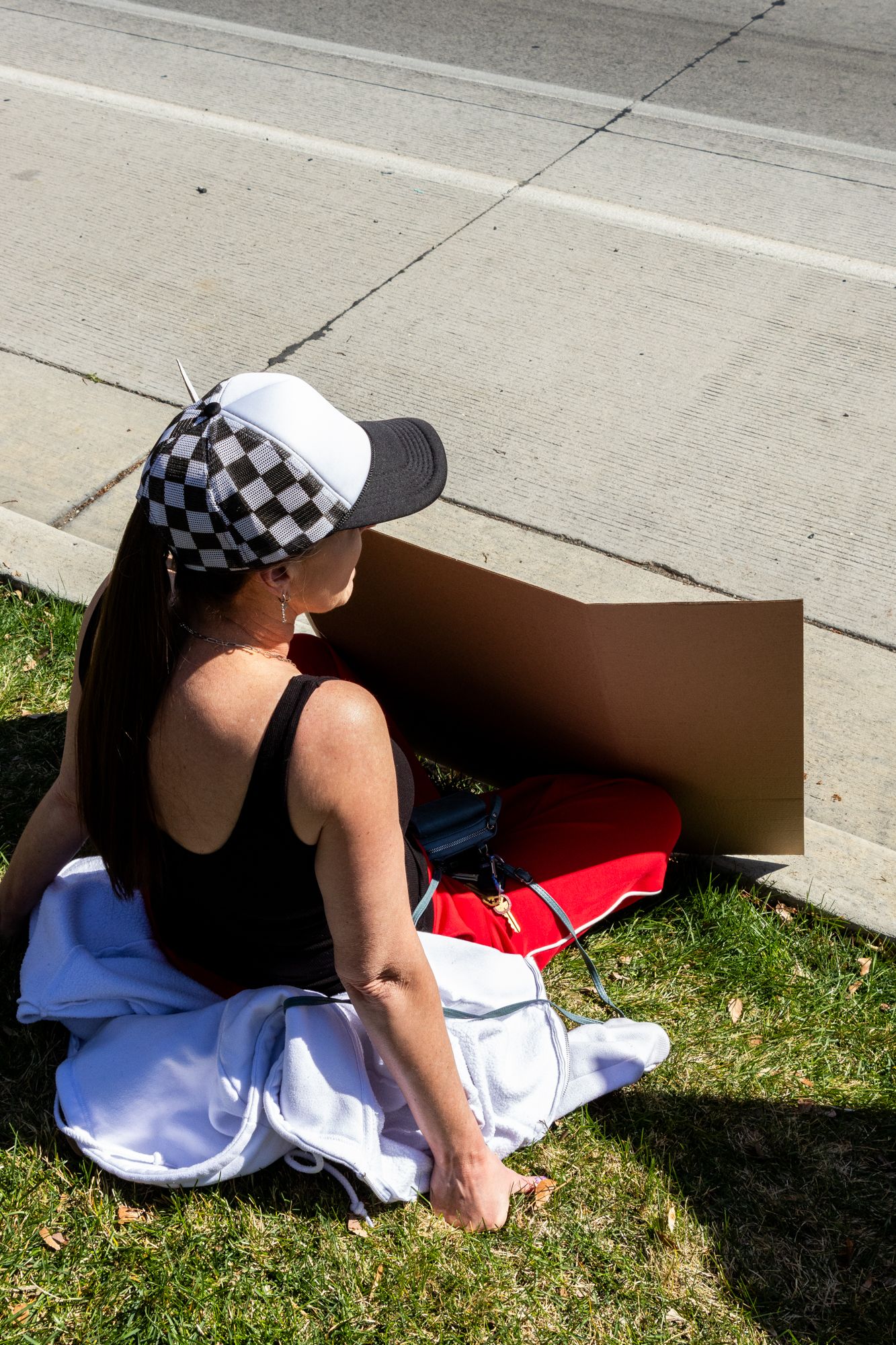 Minimal roadside portrait of a woman with cardboard sign. Quiet, sunlit moment inviting curiosity, tension, and human engagement.