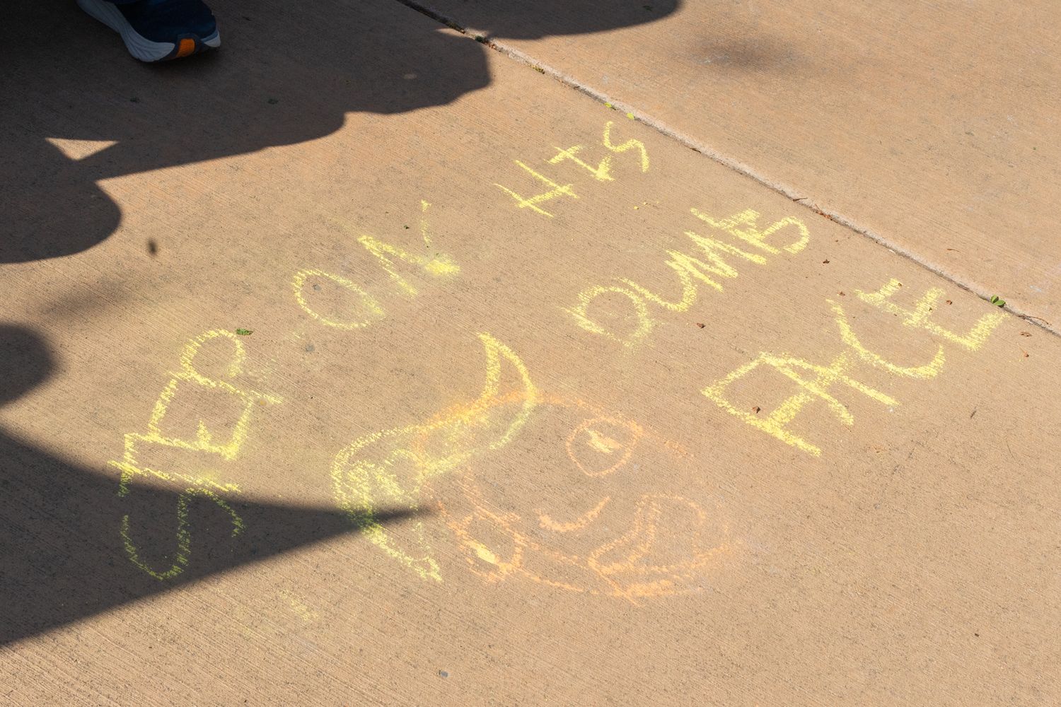 A close-up documentary shot of chalk messages on a sidewalk, framed by the feet of passersby to show the interaction  or art and crowd.