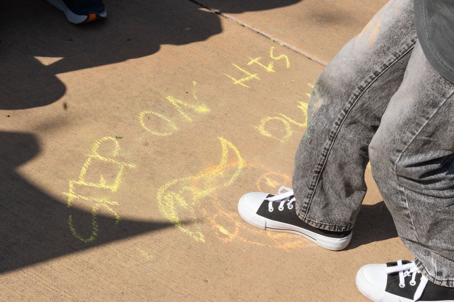 A close-up documentary shot of chalk messages on a sidewalk, framed by the feet of passersby to show the interaction  or art and crowd.