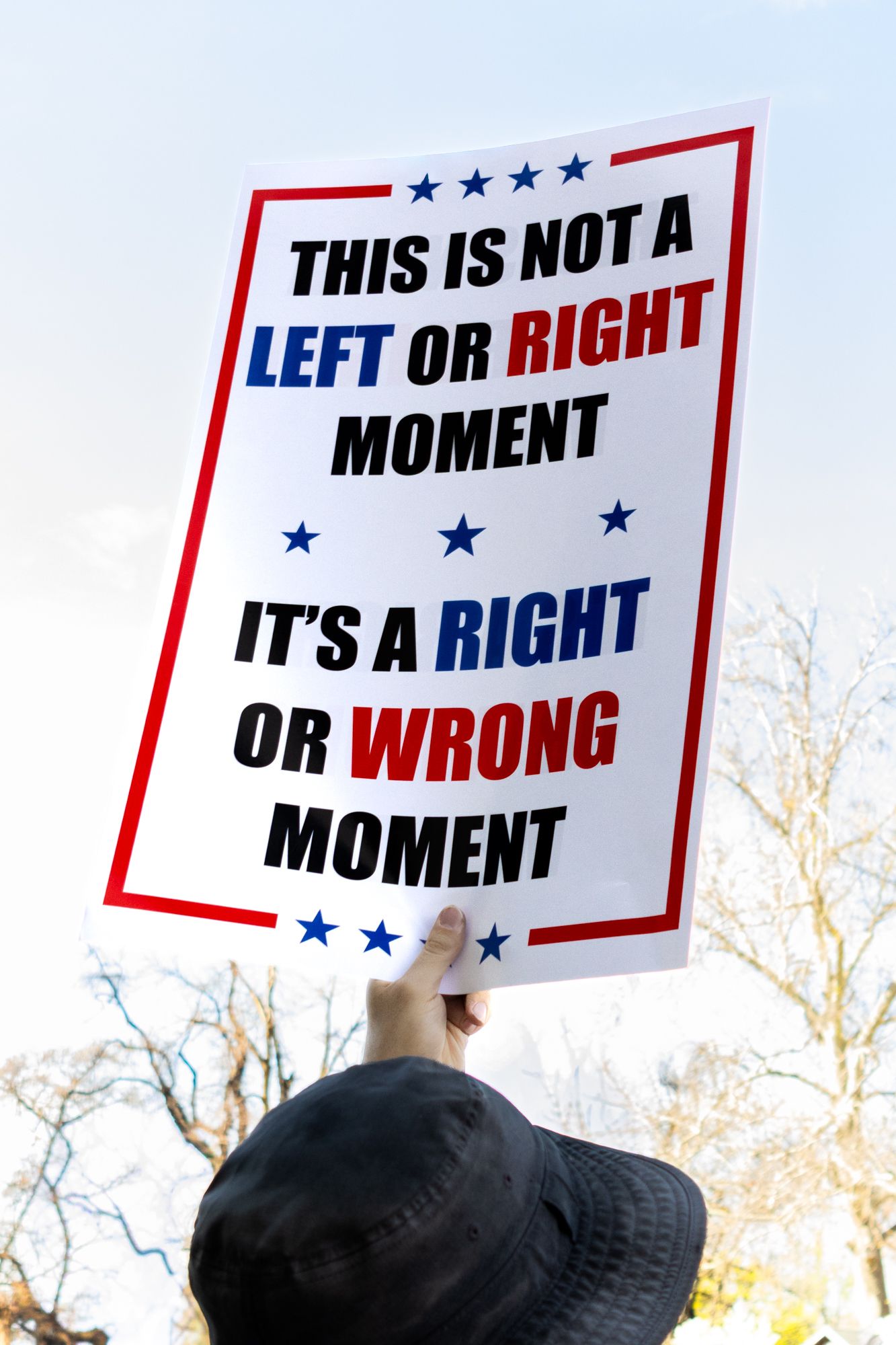 A vertical documentary shot focusing on a protest sign that highlights the moral nature of the event, held high against a clear sky.