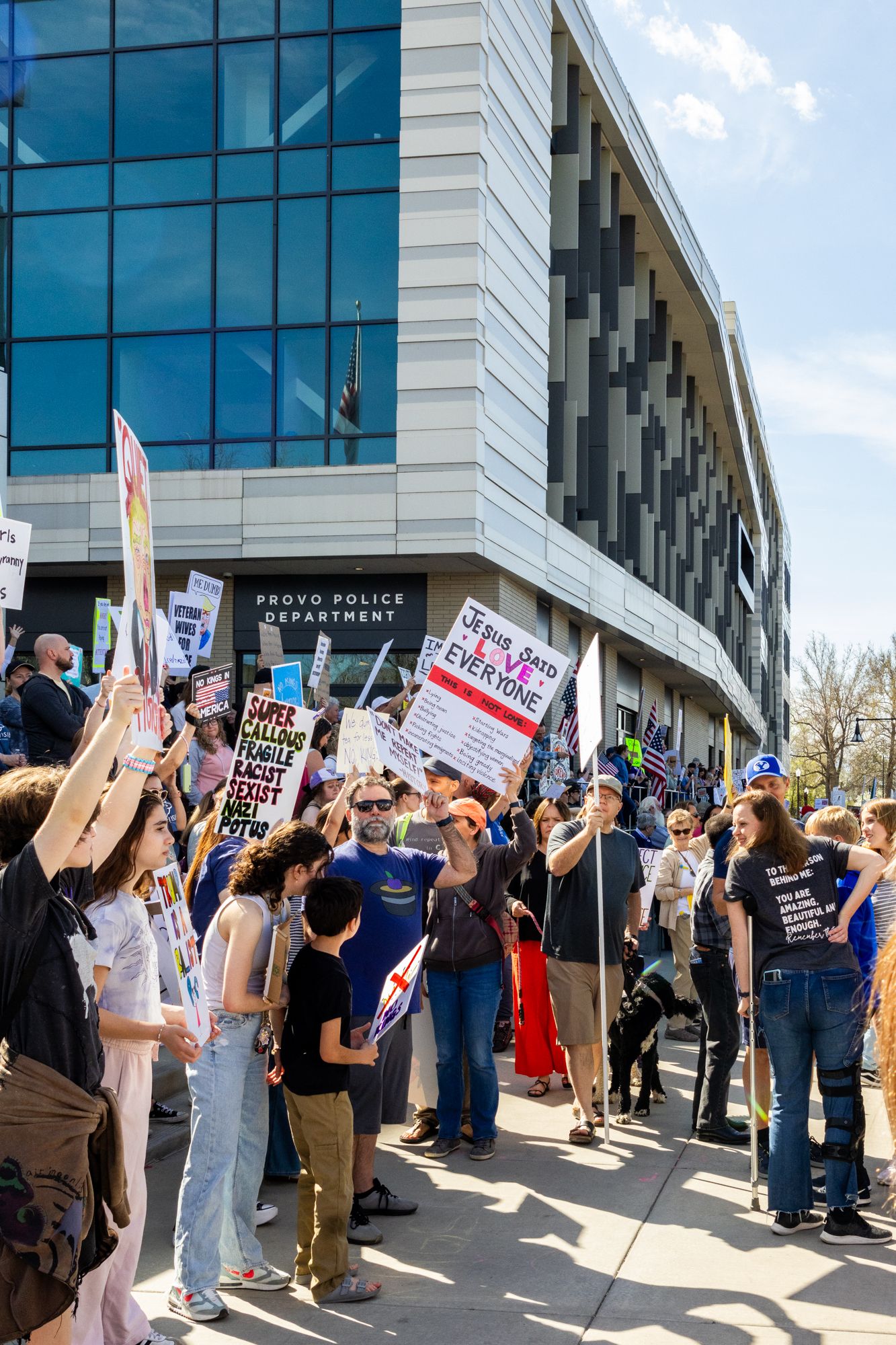 A vibrant documentary shot capturing a diverse crowd gathered for a public demonstration outside the Provo Police Department.