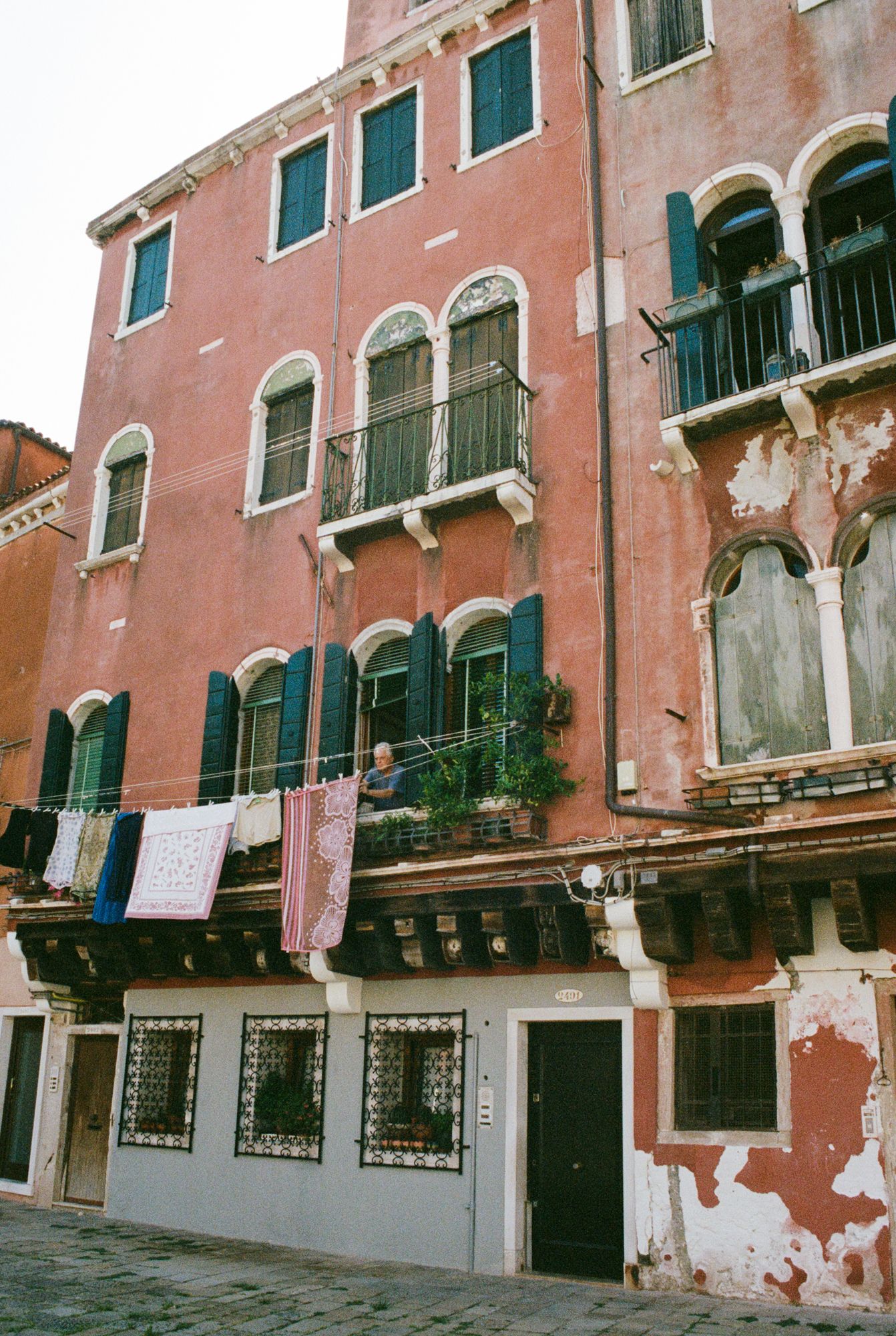 Laundry hangs from the balcony of a weathered pink palazzo in Venice, capturing the authentic daily life and charm of Italy’s canal city.