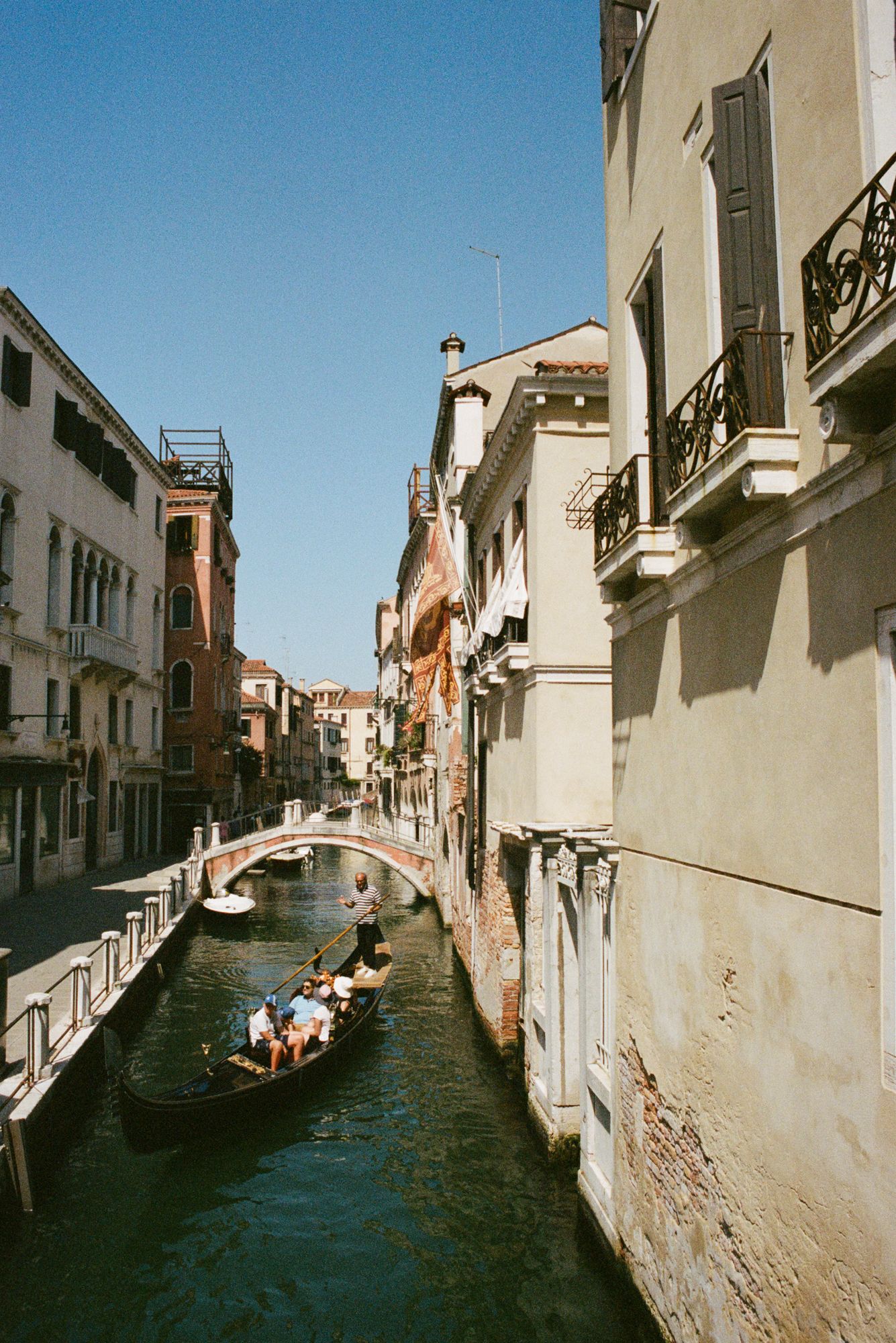 Experience the timeless romance of Venice, Italy, with a gondola gliding through a quiet canal beneath historic bridges and sunlit facades.