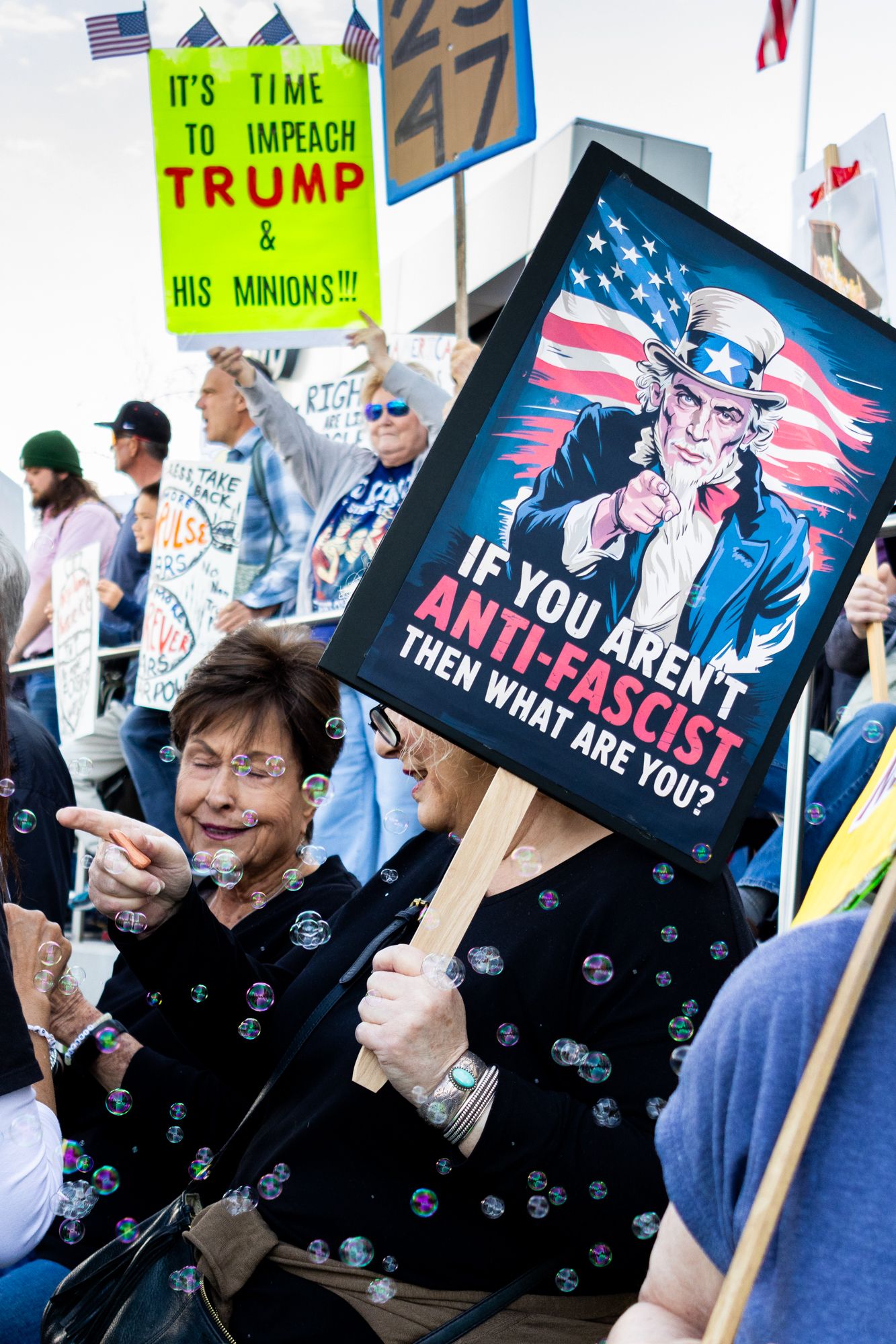 A vertical documentary shot capturing demonstrators holding bold political signs amidst a flurry of bubbles, creating a candid shot.
