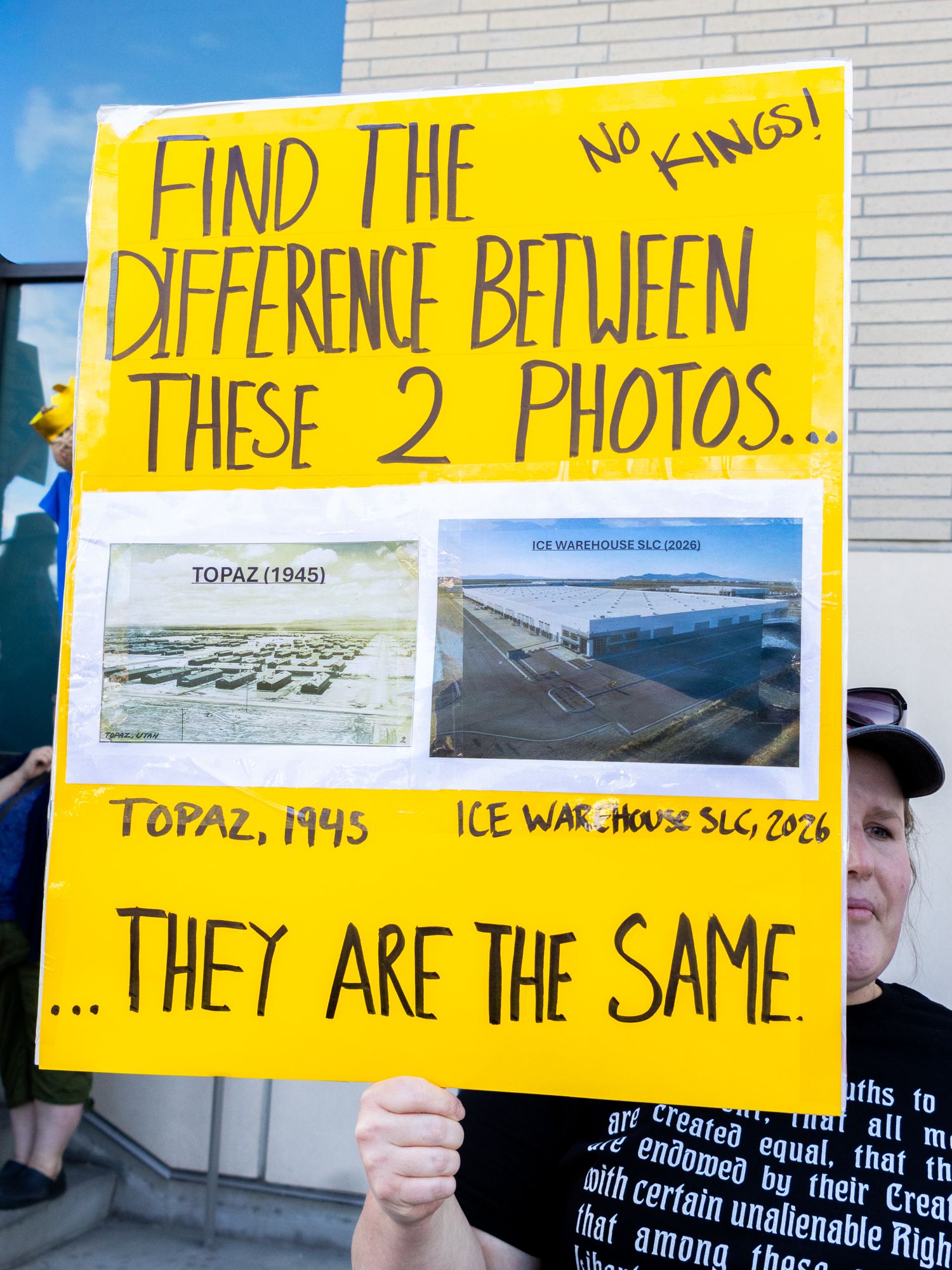 A documentary close-up of a protest sign drawing a historical parallel between Topaz 1945 and a 2026 SLC warehouse to critique ICE policy.