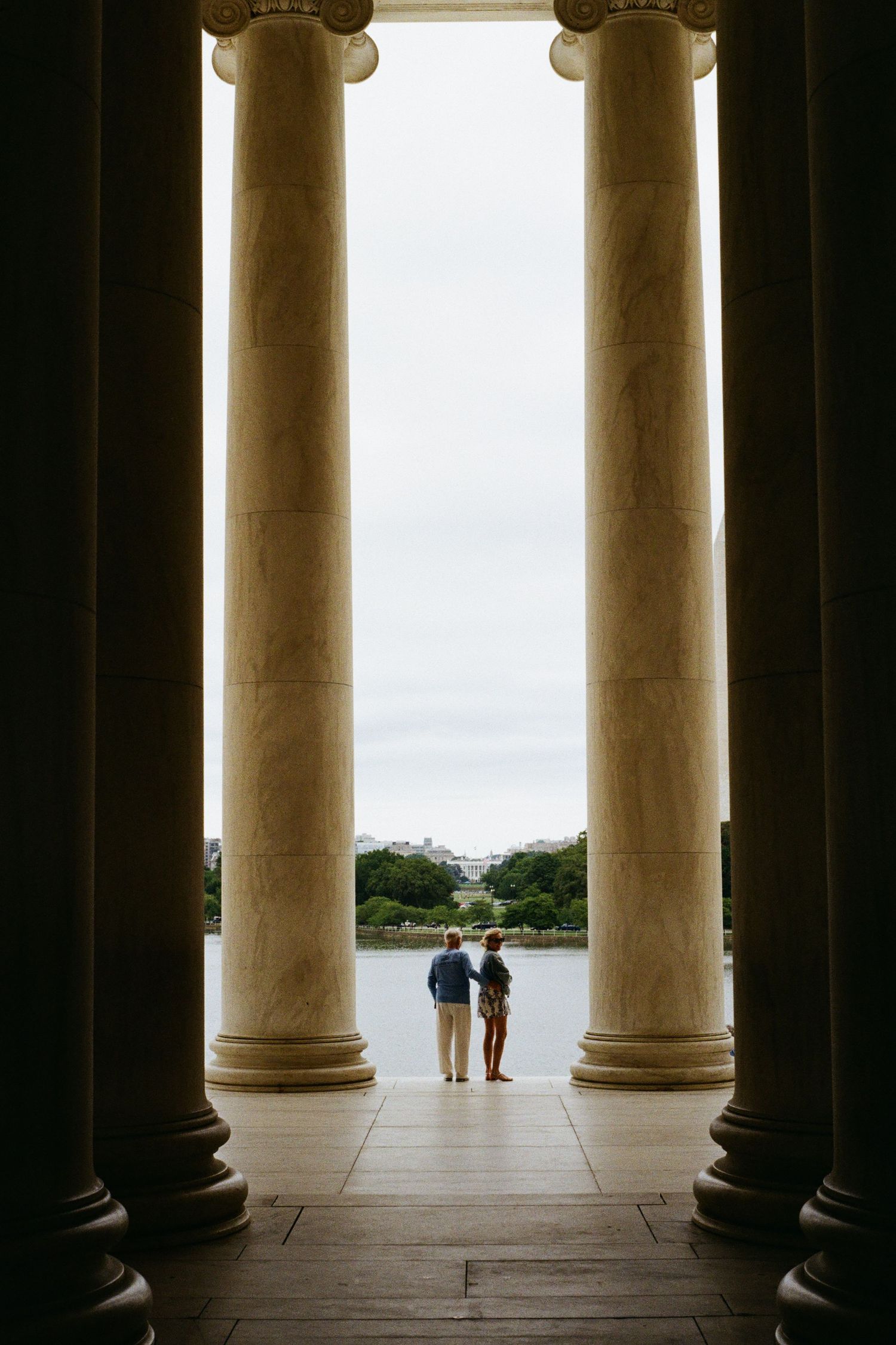 A couple gazes out at the Tidal Basin through the towering marble columns of the Jefferson Memorial, a serene moment in Washington, D.C.