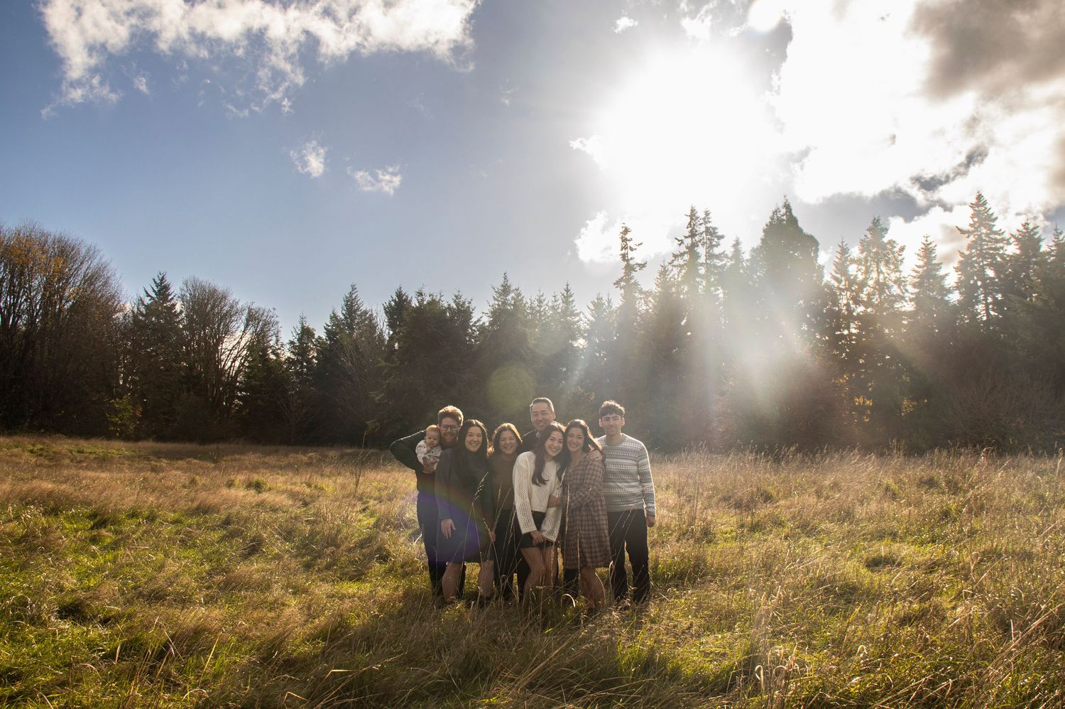 Expertly managed backlit family photography in a natural field, showcasing technical skill with lens flare for warm, authentic imagery.