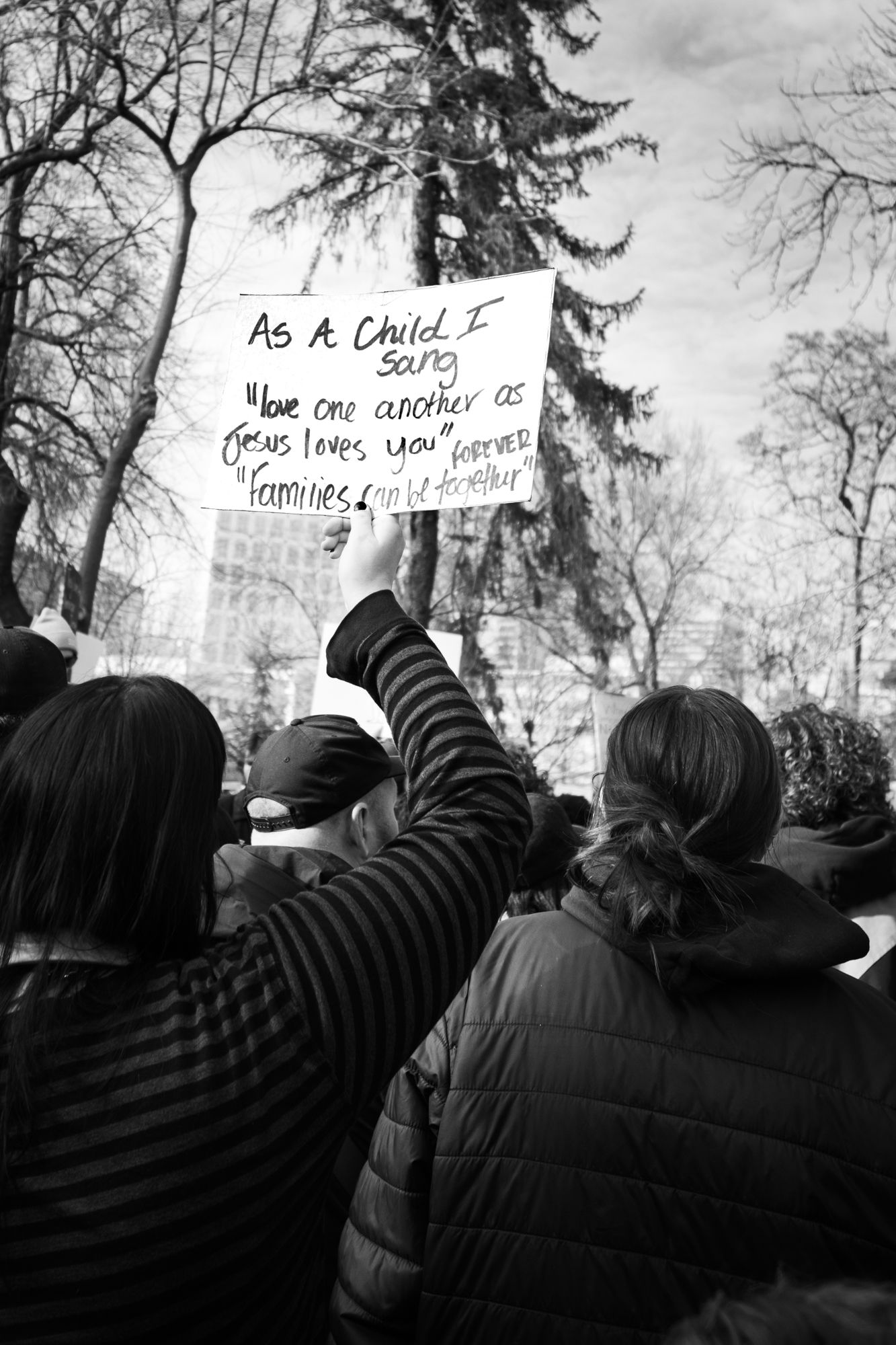Powerful B&W documentary photography of a public protest. Handwritten sign with a personal message in a city crowd. Authentic news imagery.