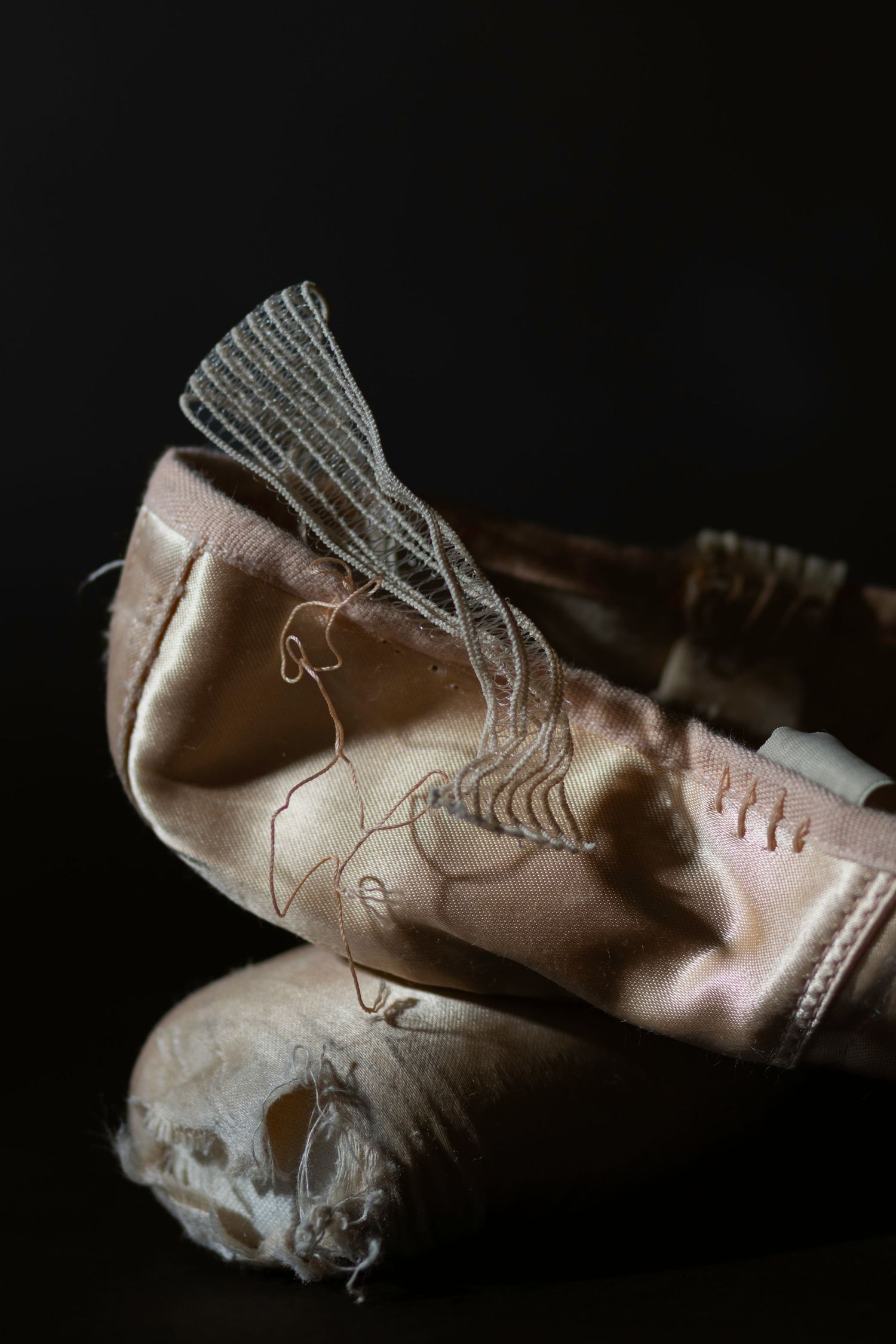 Moody macro photography of worn ballet pointe shoes. Intricate detail of frayed satin and mesh. Powerful fine art imagery for dance media.