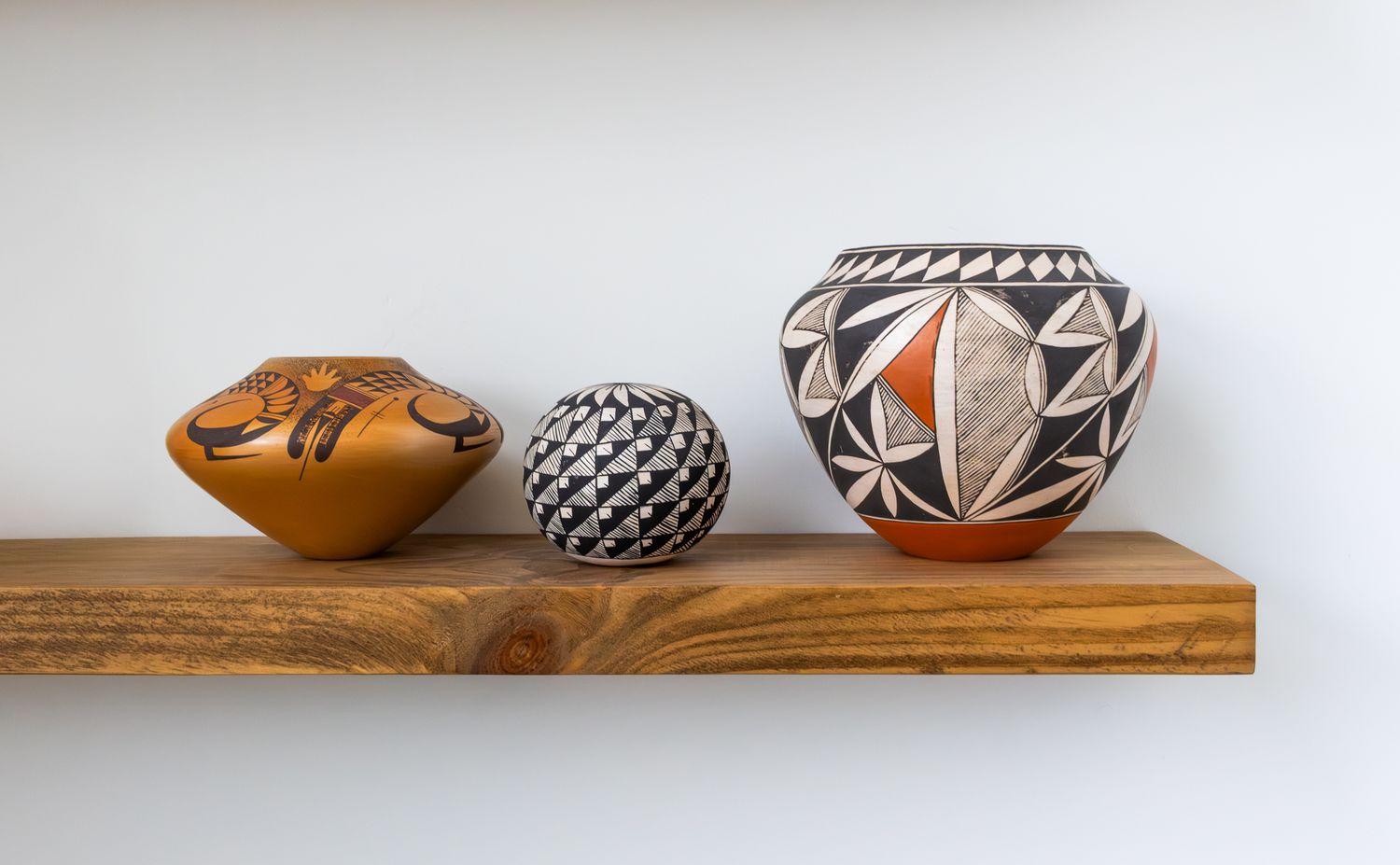Minimalist interior photography of patterned Southwestern pottery on a natural wood shelf, featuring clean lines and bright gallery lighting