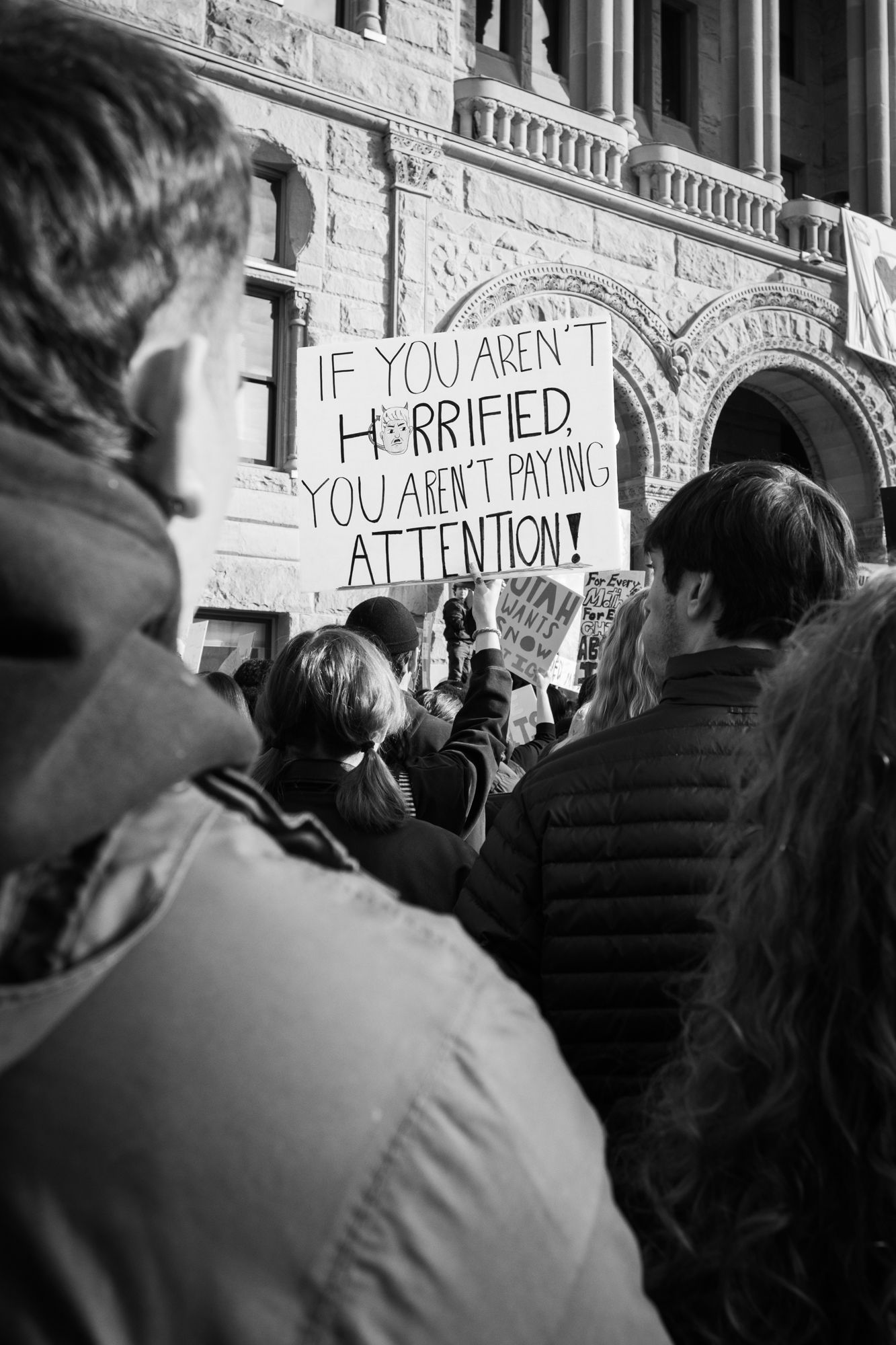 Powerful B&W documentary photography of a public protest. Handwritten sign with a personal message in a city crowd. Authentic news imagery.