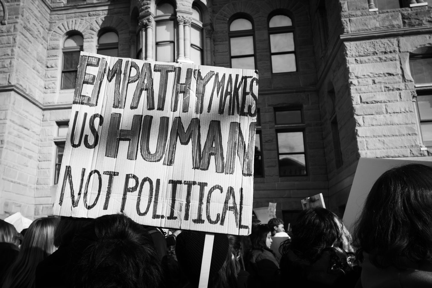Powerful B&W documentary photography of a public protest. Handwritten sign with a personal message in a city crowd. Authentic news imagery.