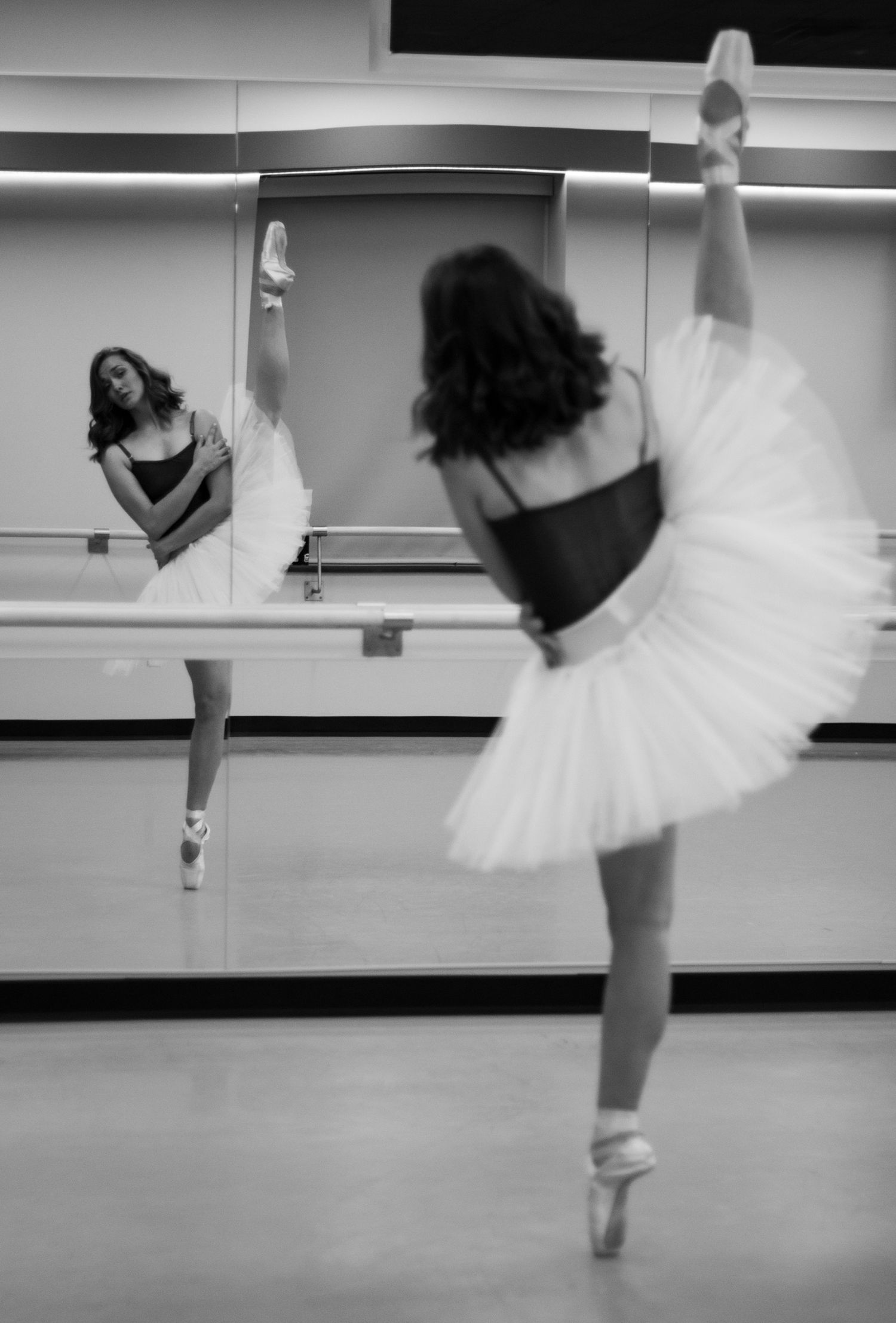 Reflections of poise. A classic en pointe extension captured in the studio mirror, highlighting the symmetry and dedication of the craft.