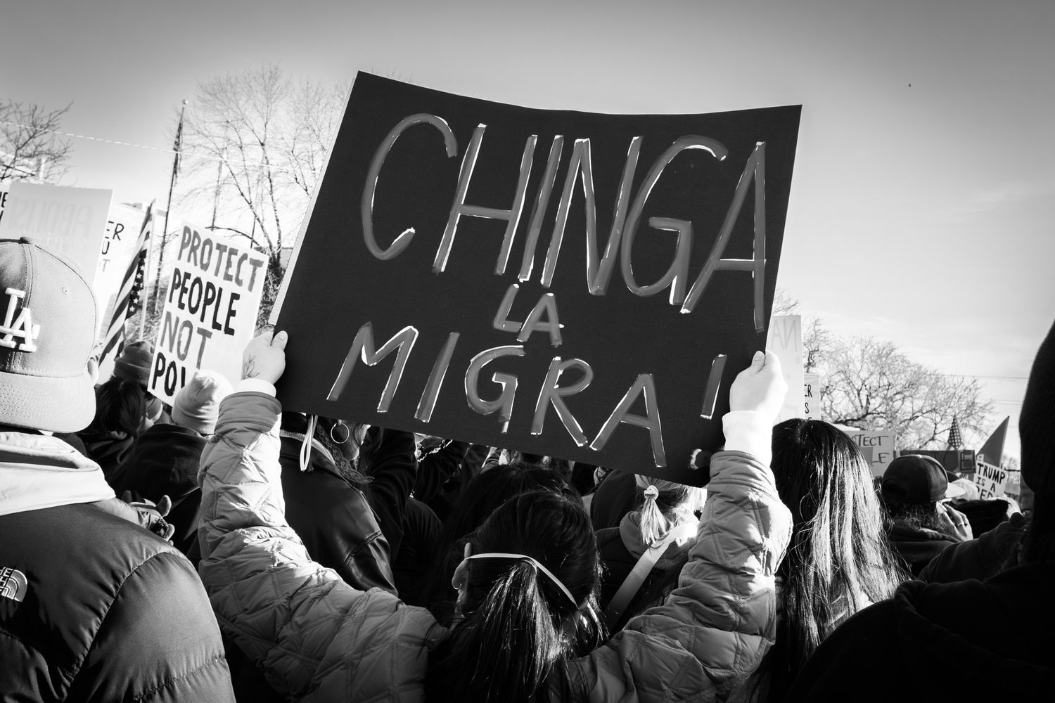 Powerful B&W documentary photography of a public protest. Bold handwritten sign in a city crowd. Authentic imagery for news and editorial.