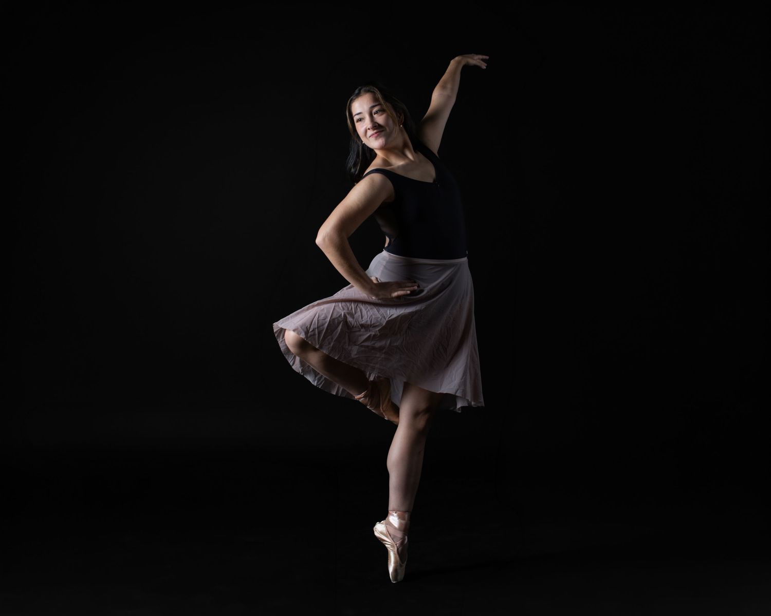 Professional ballet studio photography. Elegant dancer in a leotard and skirt on black. High-quality imagery for dance resumes and schools.