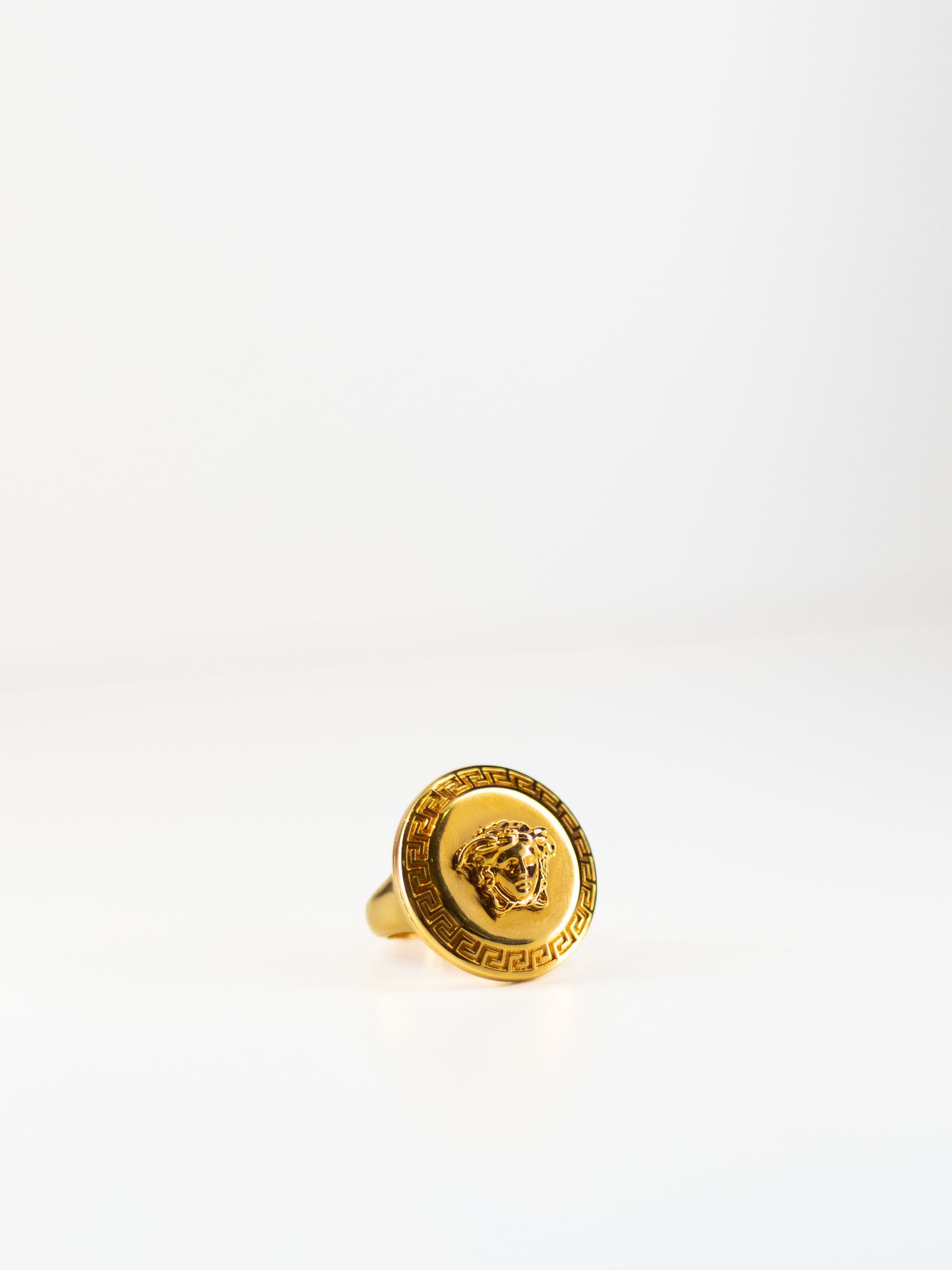 Luxury jewelry photography of a gold Versace Medusa ring, featuring clean high-key lighting and sharp detail for e-commerce and branding.