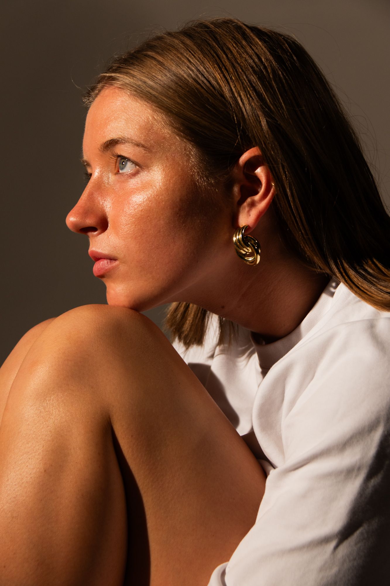 Elegant profile portrait with warm, dramatic lighting, showcasing jewelry detail and high-end skin retouching for and fashion and branding
